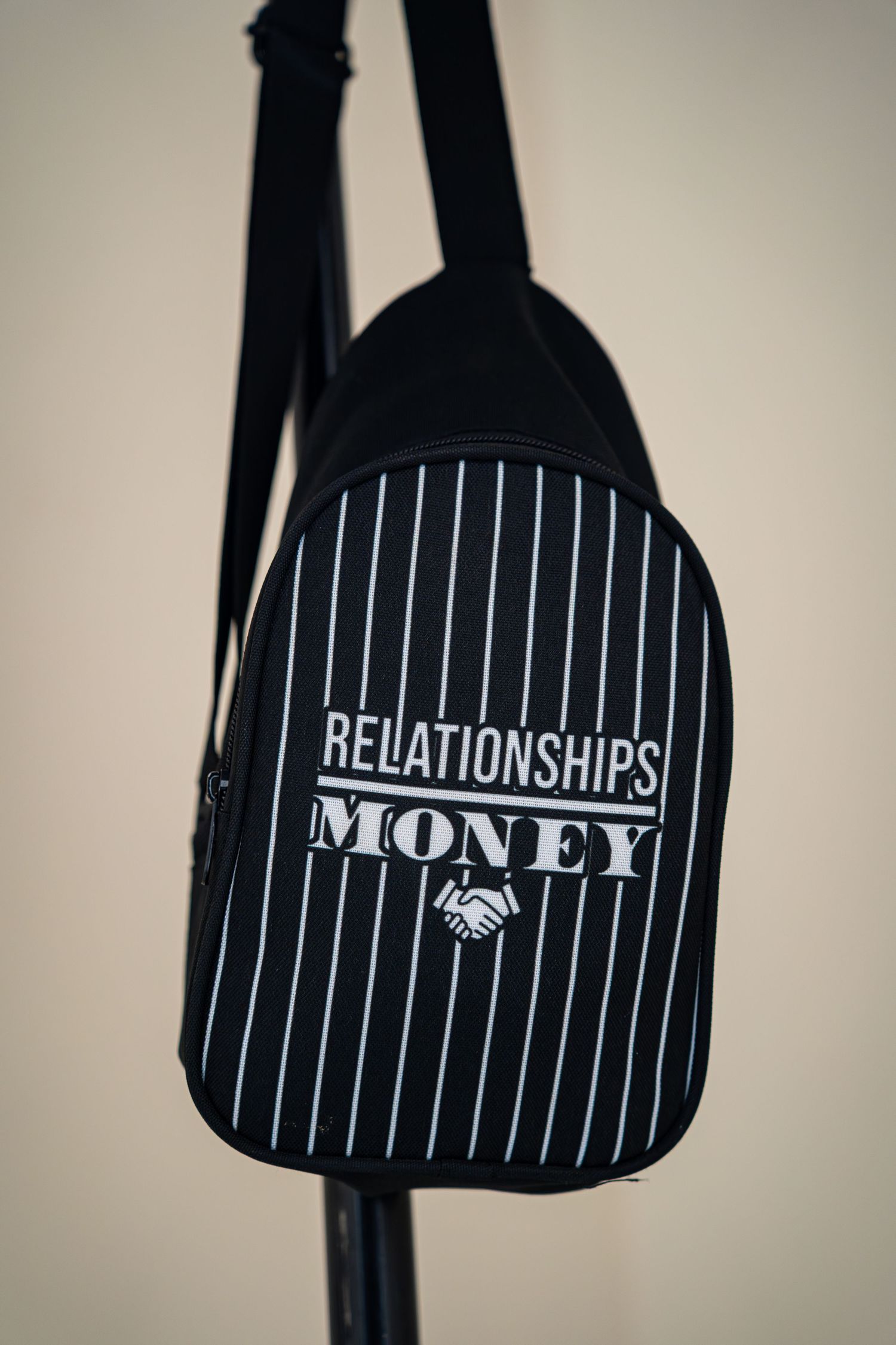 Black pinstripe backpack with Relationships Over Money slogan hanging on a rack.