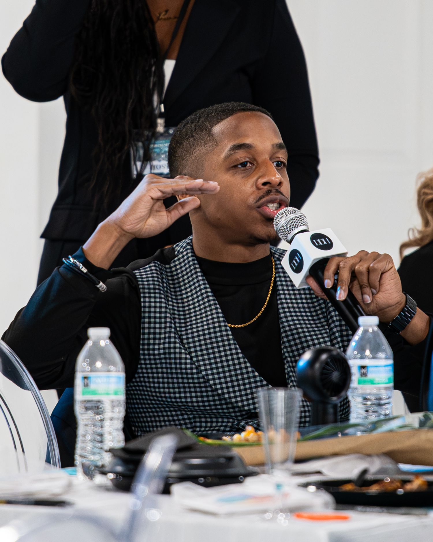 Man in houndstooth vest speaks into microphone at entrepreneur panel discussion event.