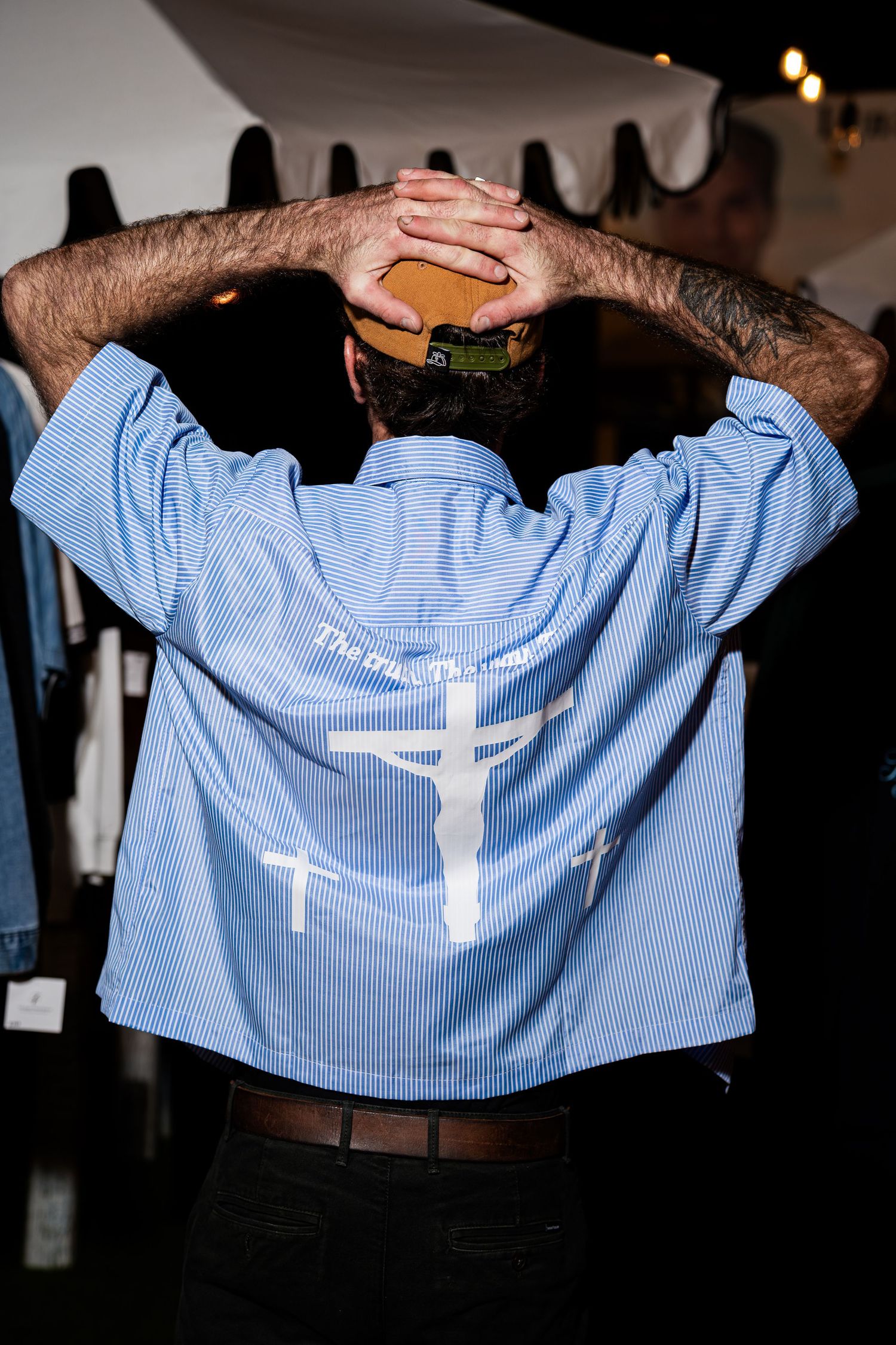 Back view of blue striped shirt featuring crucifixion cross graphic design at night market.