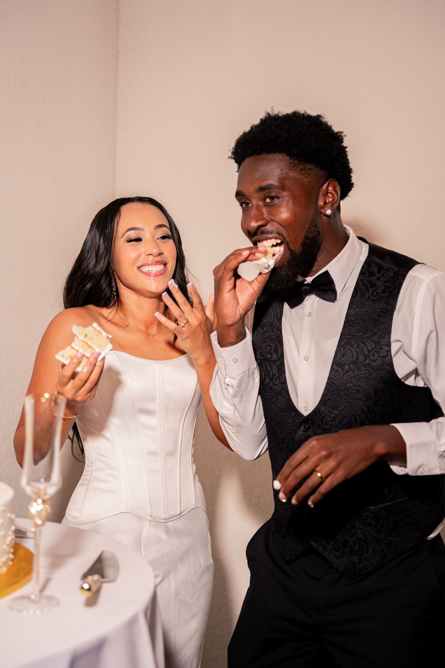 Bride and groom laugh while cutting and tasting wedding cake at their reception celebration.