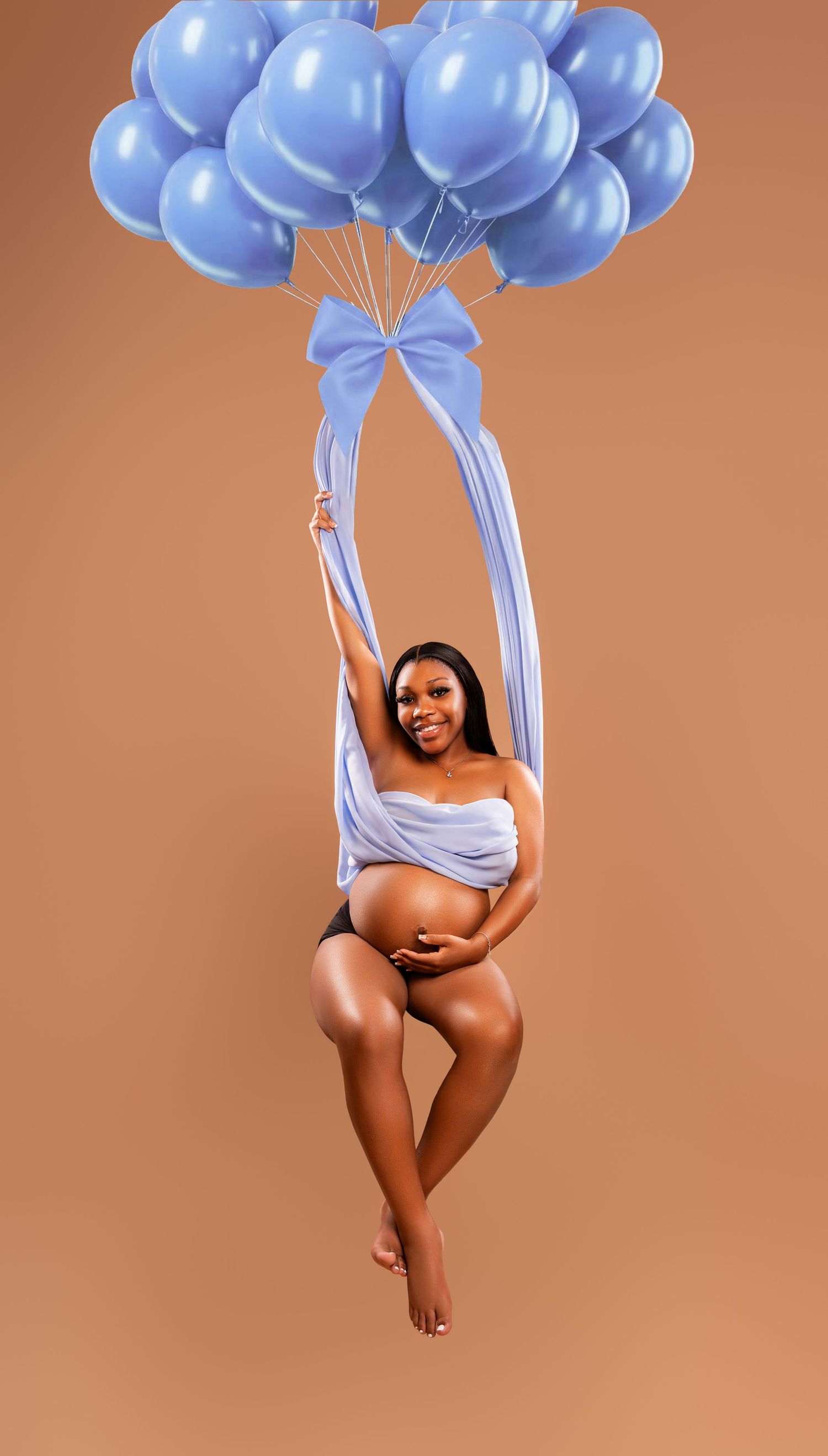 Pregnant woman in blue fabric wrap poses with blue balloons in a maternity photo shoot against brown background.