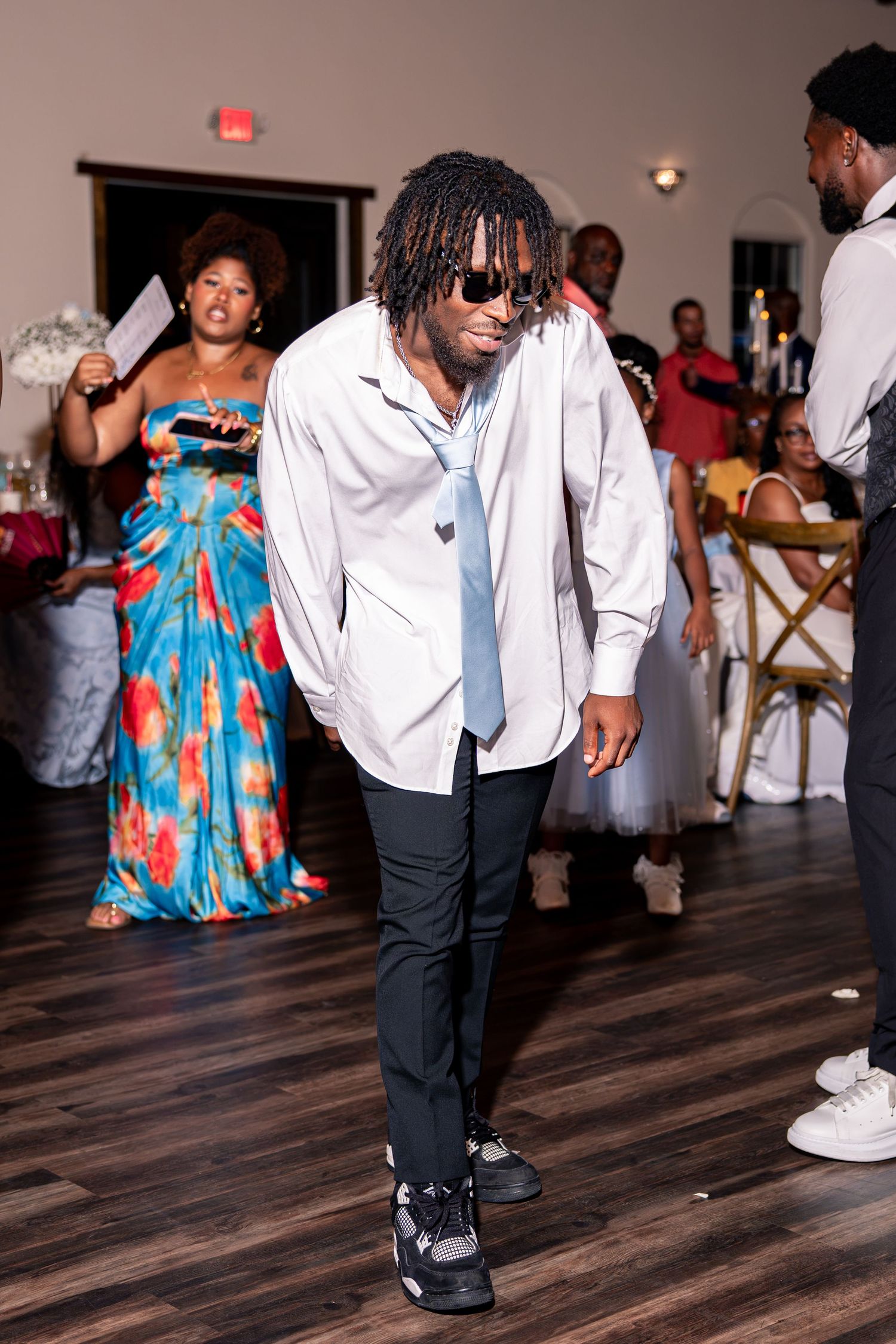 Wedding guest in white shirt and sunglasses dances energetically on dance floor at wedding reception.