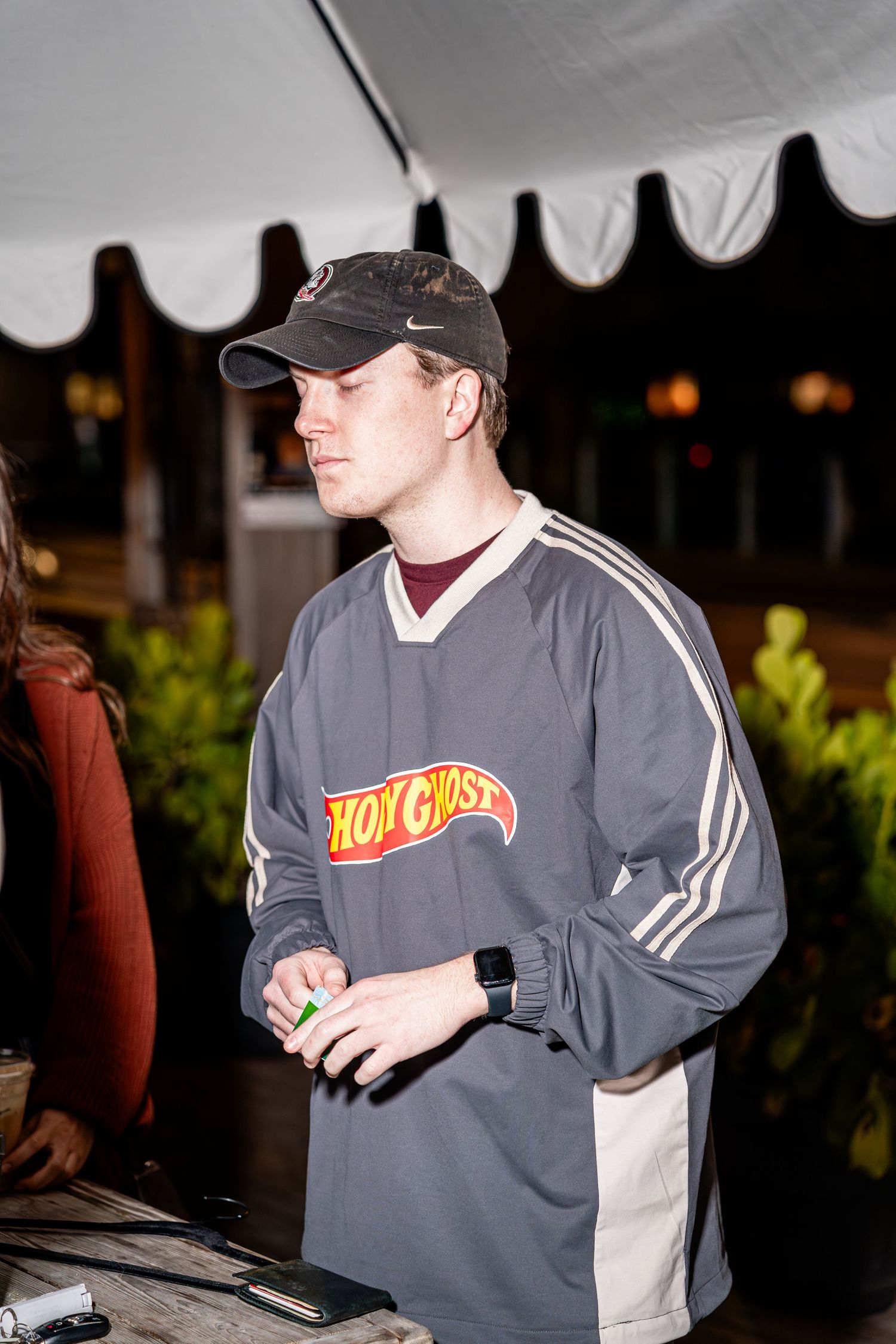 Young man wearing Hot Ghost branded gray hockey jersey at outdoor night market event.