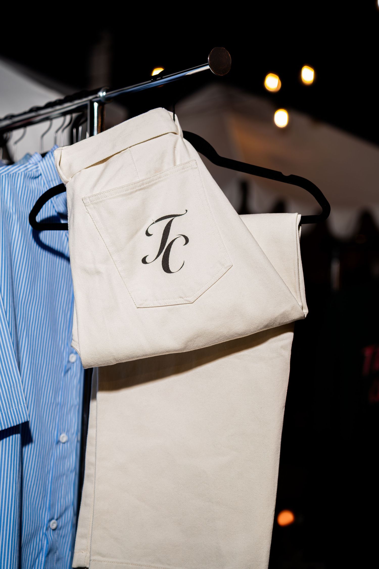 White pants with TC monogram logo on pocket displayed on a clothing rack at Through Christ Brand.