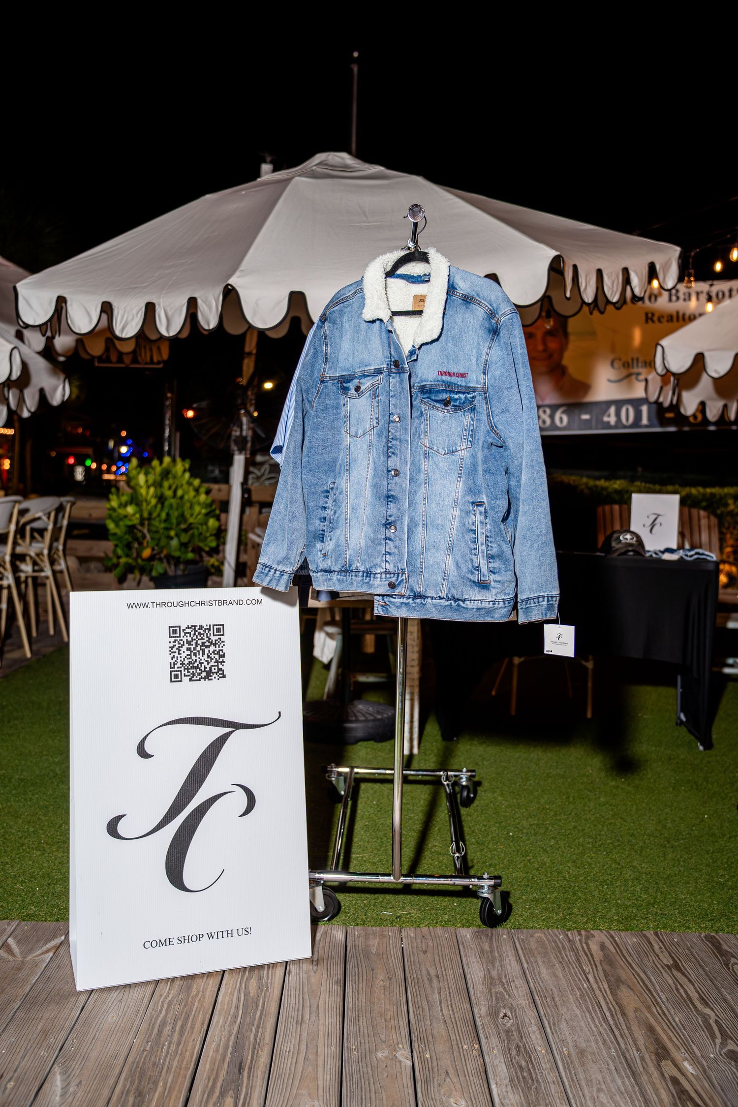 Light wash denim jacket with sherpa collar on display rack with TC brand sign at night market.