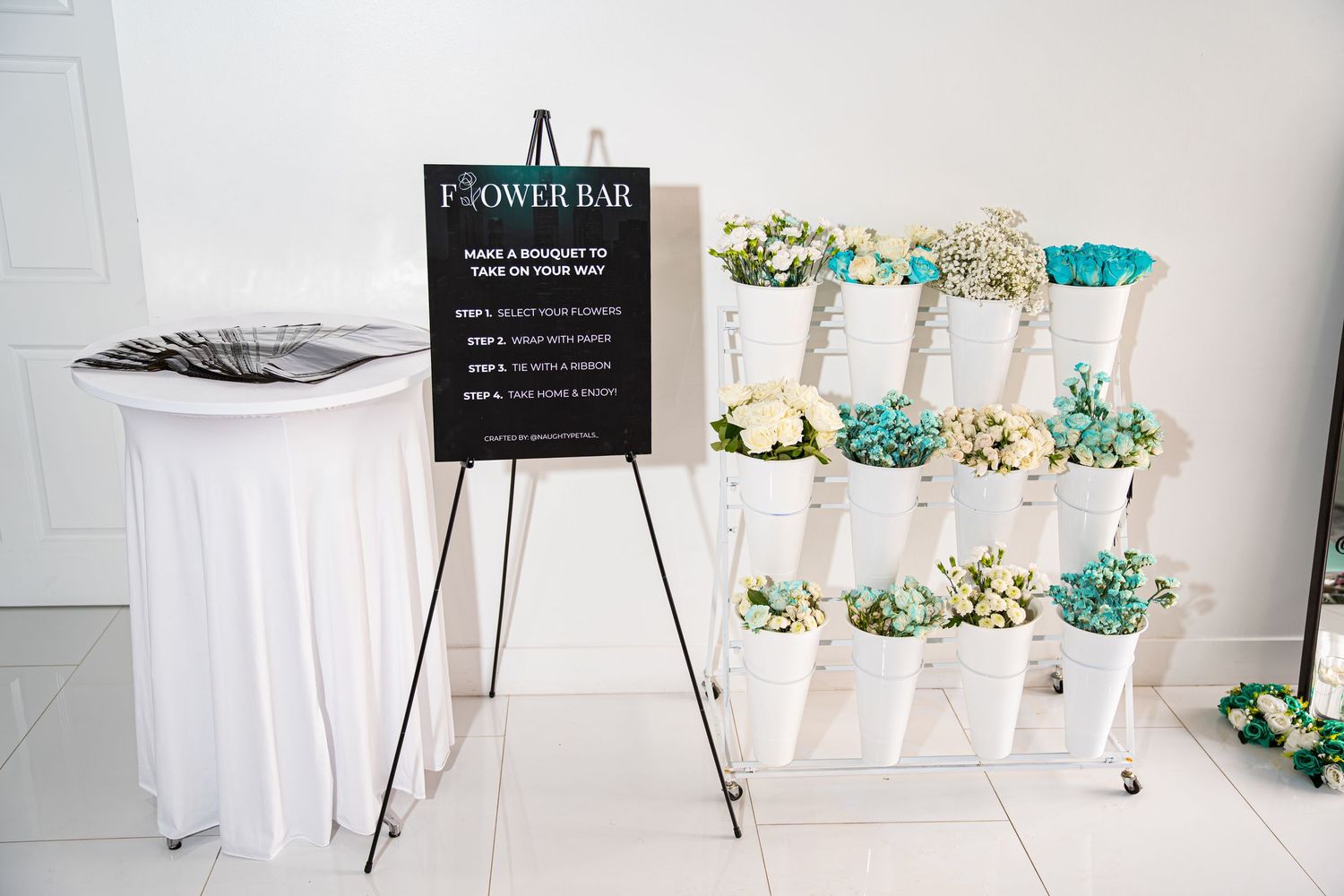 A white flower bar display stand with teal and white floral arrangements at a networking event.