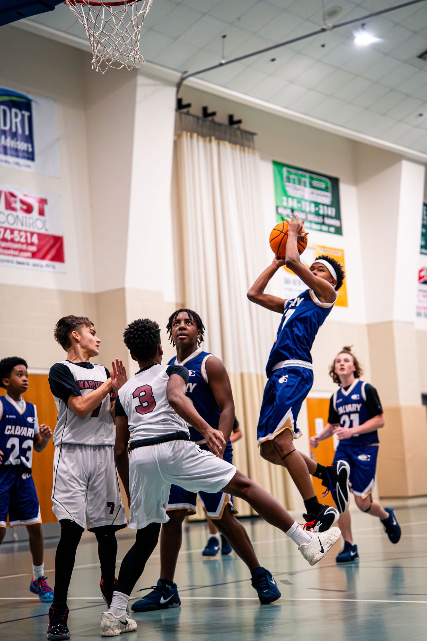 Calvary player #11 drives to basket for layup attempt against multiple defenders during indoor game.