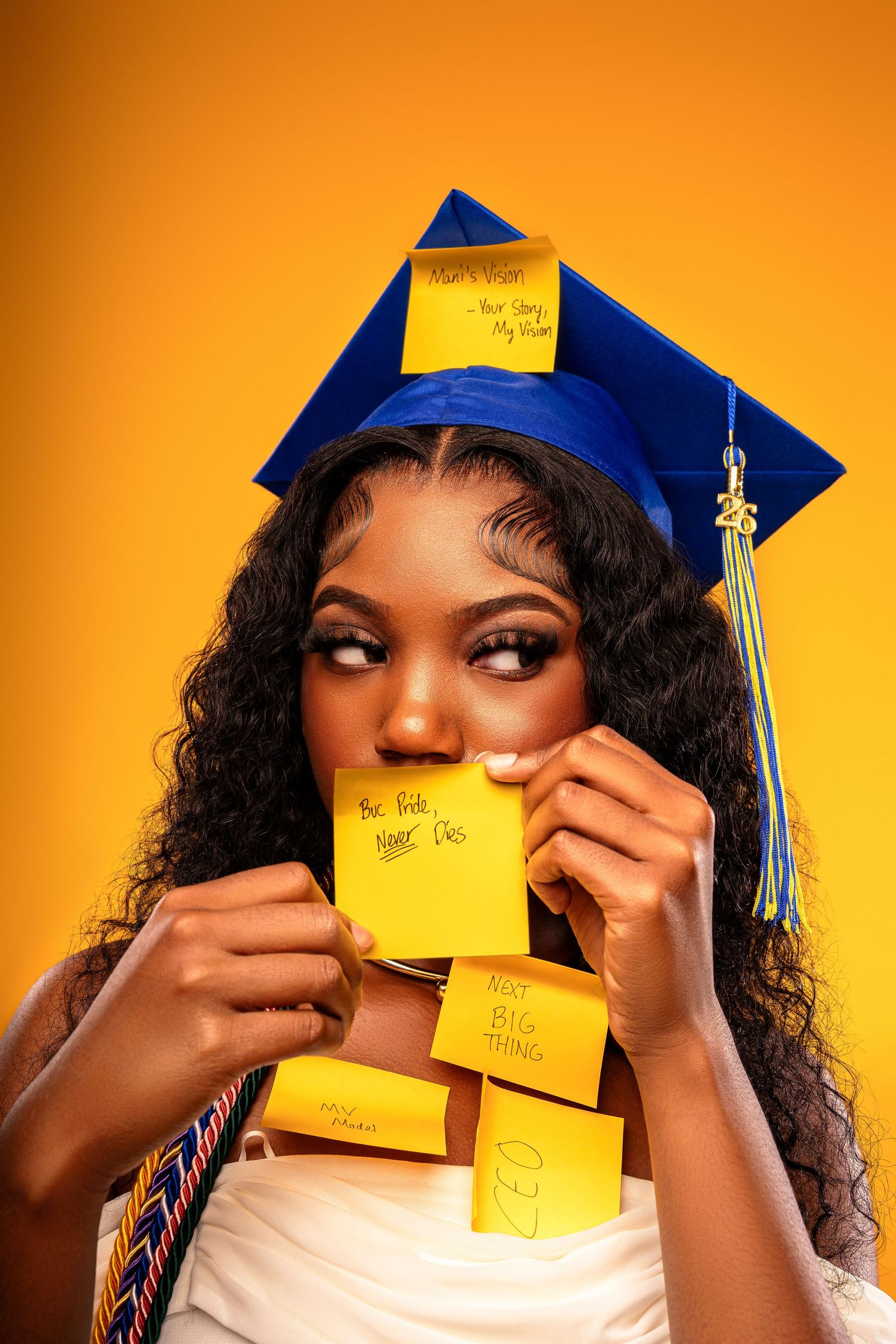 Young Black woman in blue graduation cap covered in yellow sticky notes with motivational phrases on orange background.