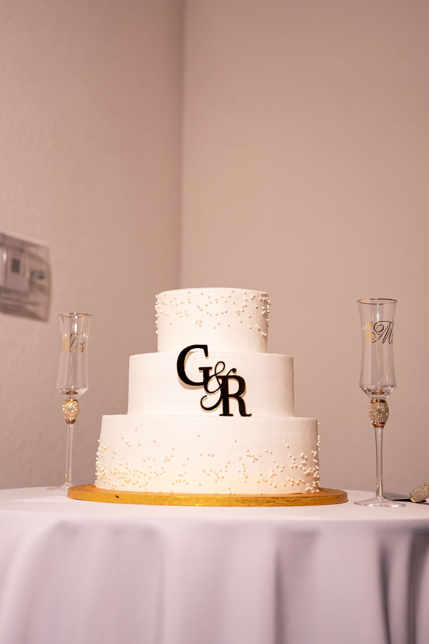 Elegant three-tier white wedding cake with G&R monogram topper flanked by champagne flutes.