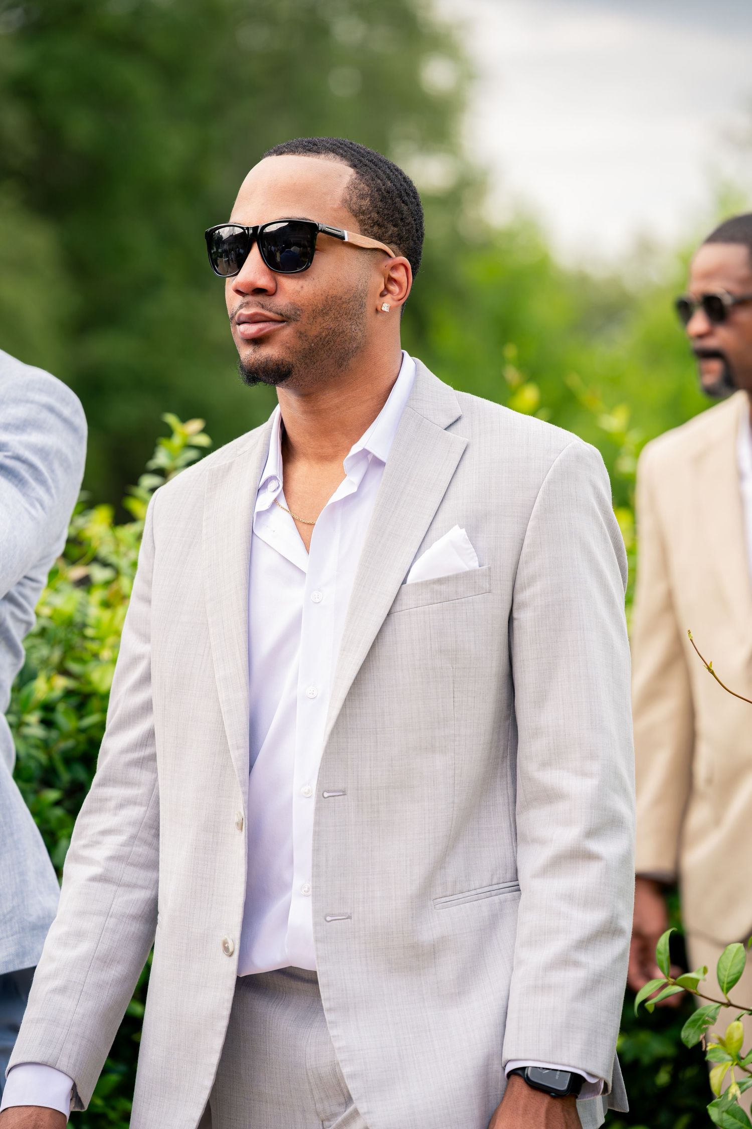 Stylish man in light gray suit and sunglasses at an outdoor wedding event.