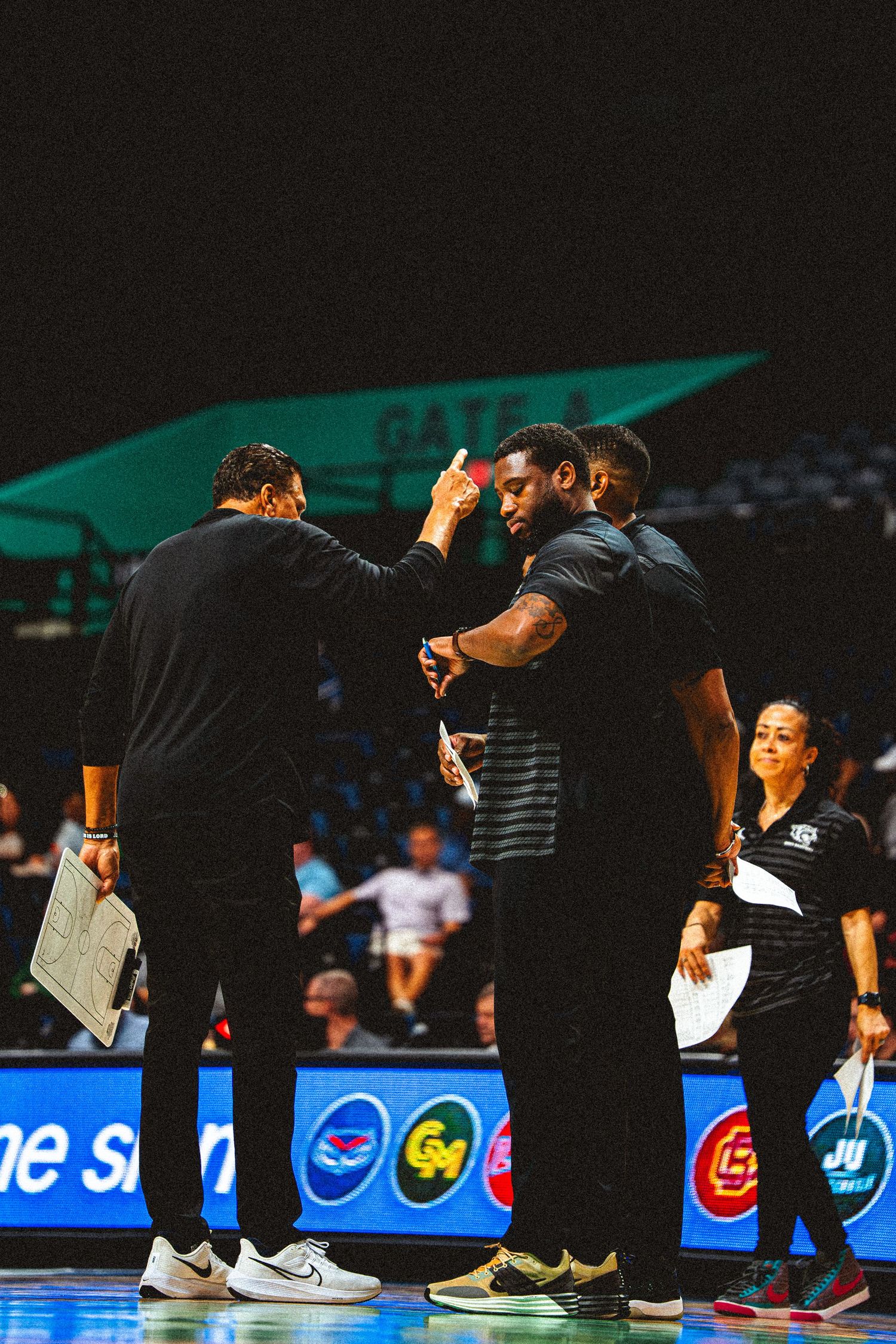 Basketball coaches review strategy with a player on the sideline during a college game.