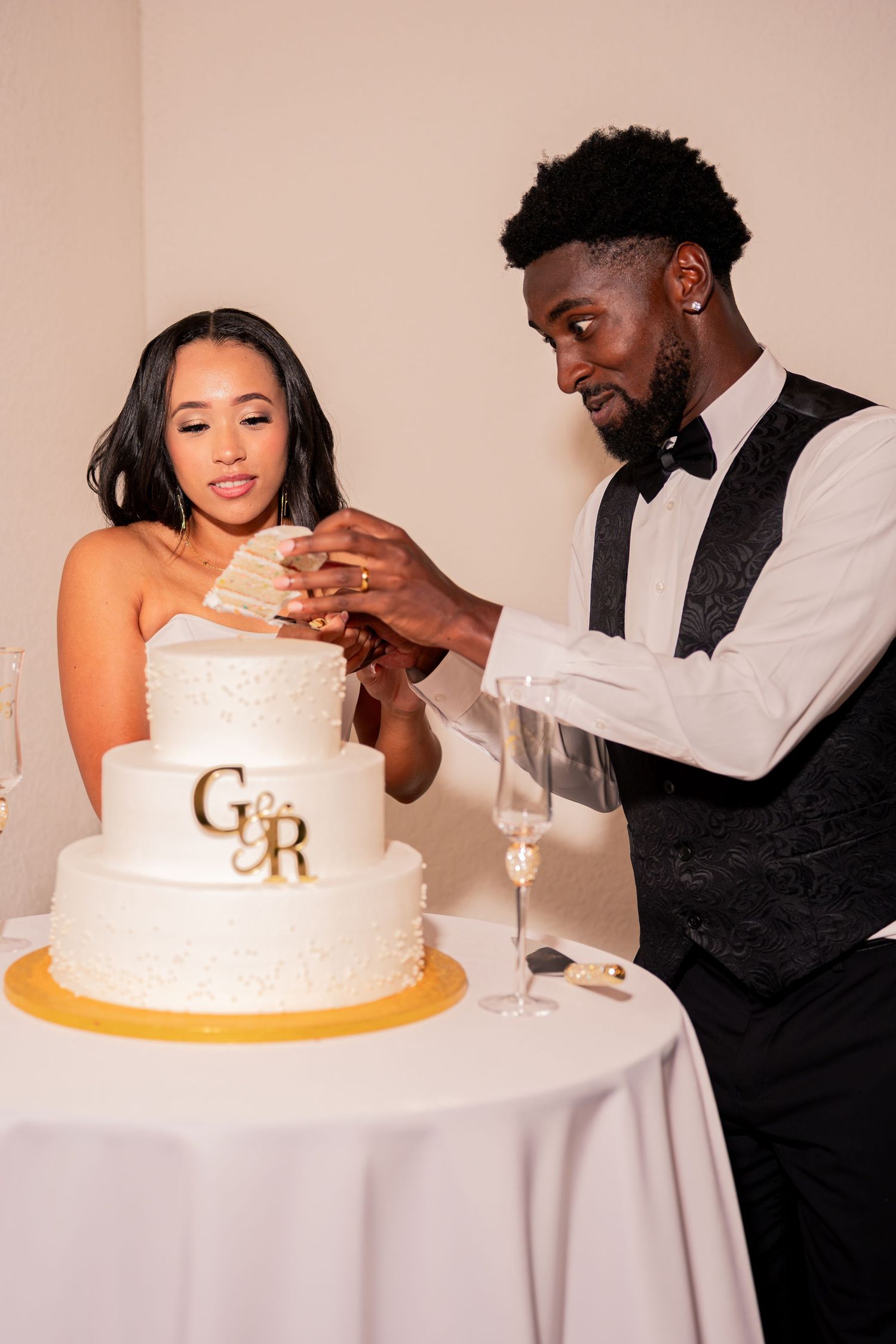 Bride and groom cutting three-tier white wedding cake with gold G&R monogram topper.