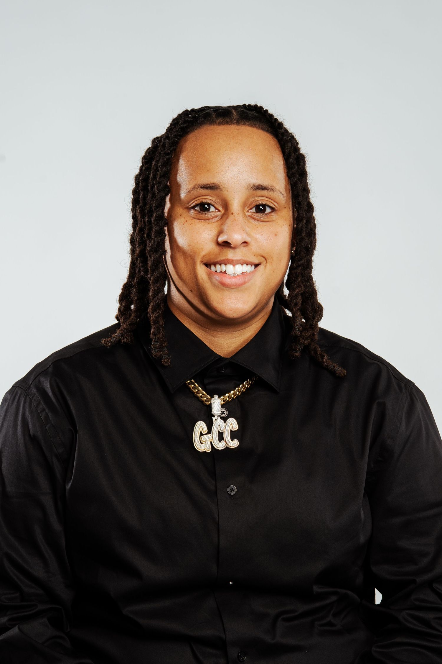 Smiling person with dreadlocks wearing black satin shirt and GCC gold chain necklace.