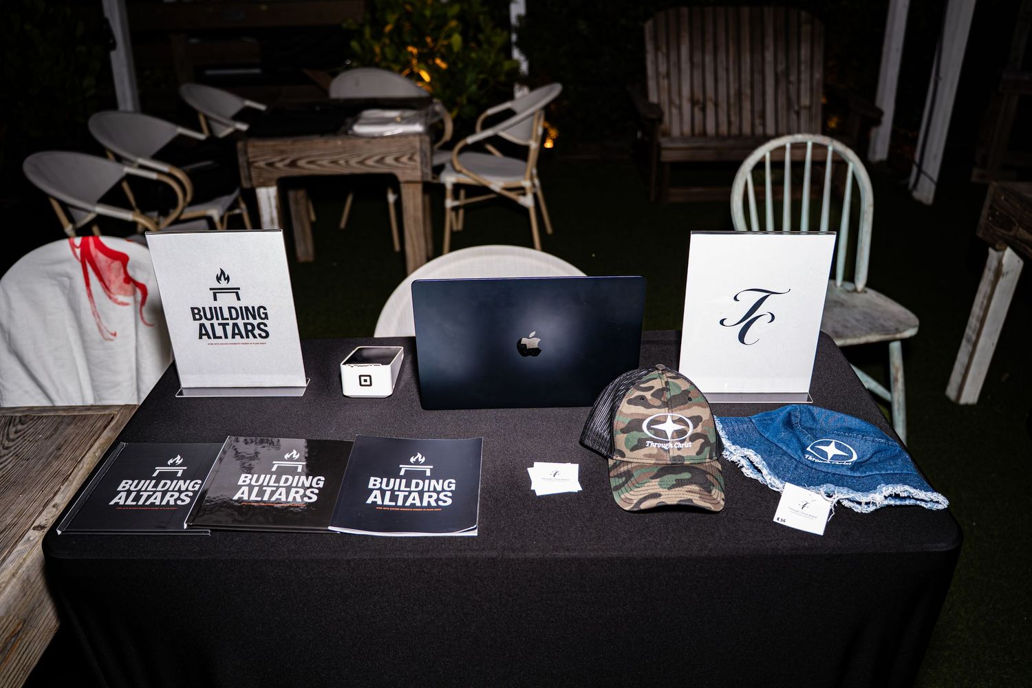 Building Altars books and TC branded caps arranged on black table with laptop at event.