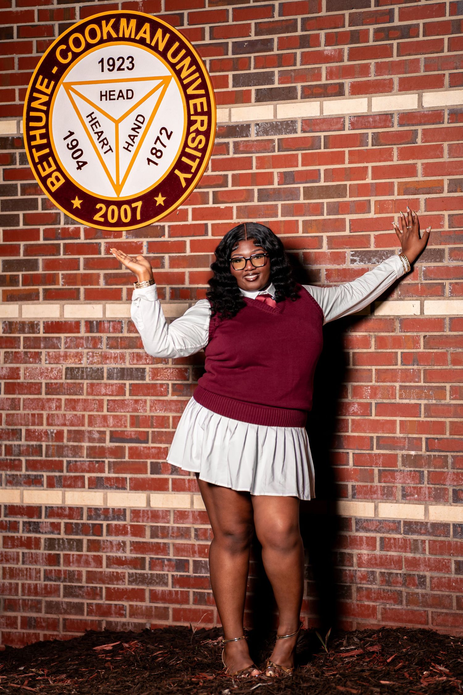 A young Black woman poses proudly beside the Bethune-Cookman University seal on a brick wall.