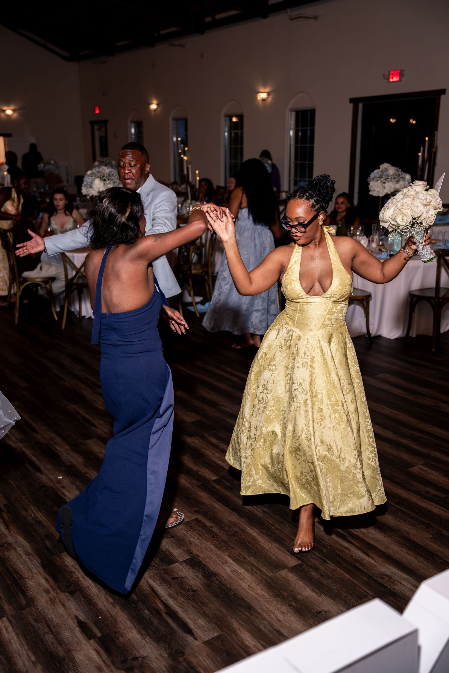 Guests dance energetically at wedding reception, woman in gold dress holds bouquet on dance floor.