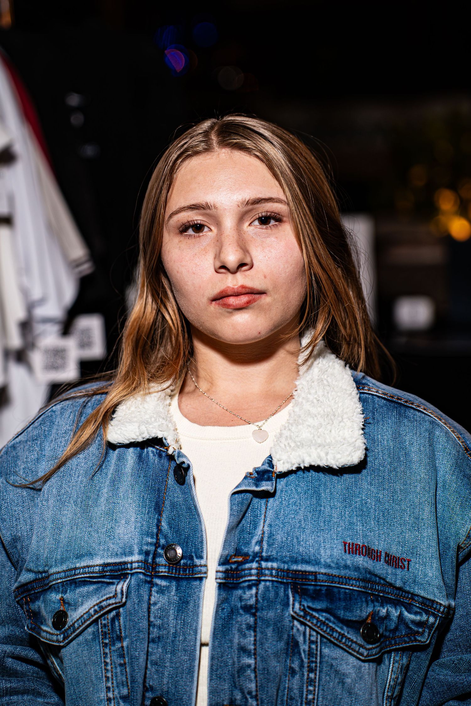 Portrait of young woman in Through Christ Brand denim jacket at outdoor night event.