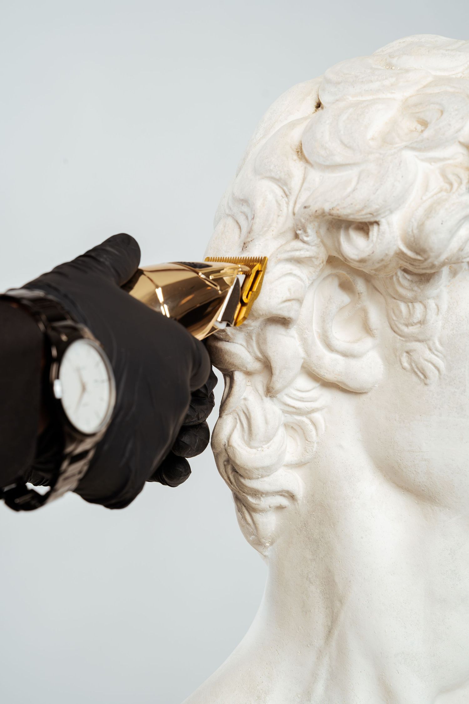 Close-up of gloved hand with watch using gold clippers on white marble bust.