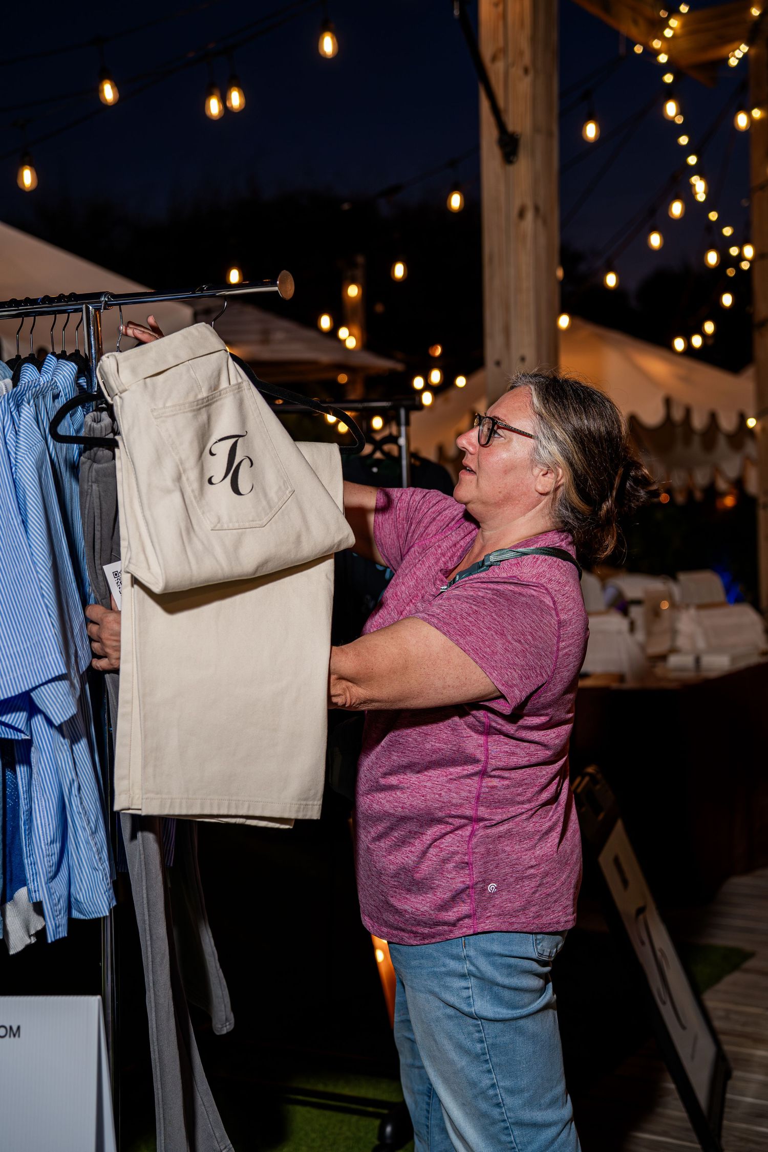 Woman examining white TC monogram pants on a rack at Through Christ Brand pop-up shop.