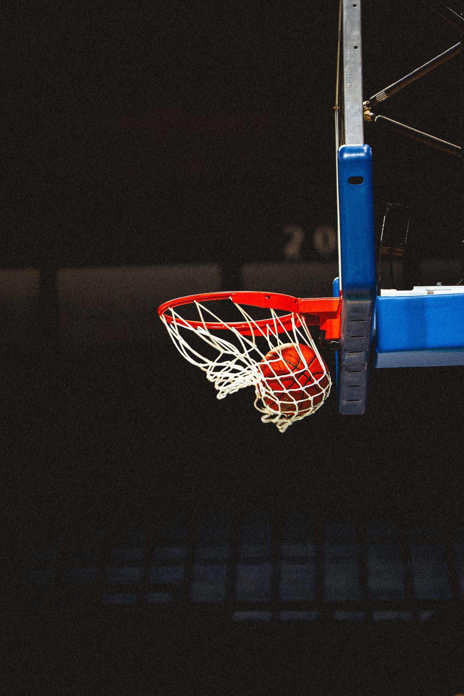Basketball passing through illuminated orange hoop and white net against dark arena background.