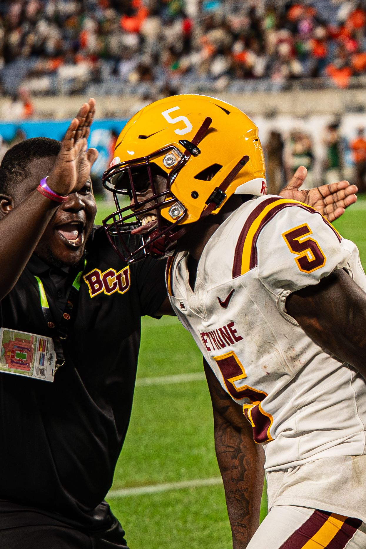 Bethune-Cookman player #5 celebrates with a BCU staff member on the sideline during a game.