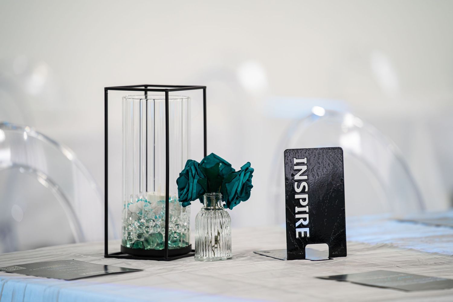 Elegant event table centerpiece with teal flowers, glass vase, and black Inspire sign at The Valentine venue.
