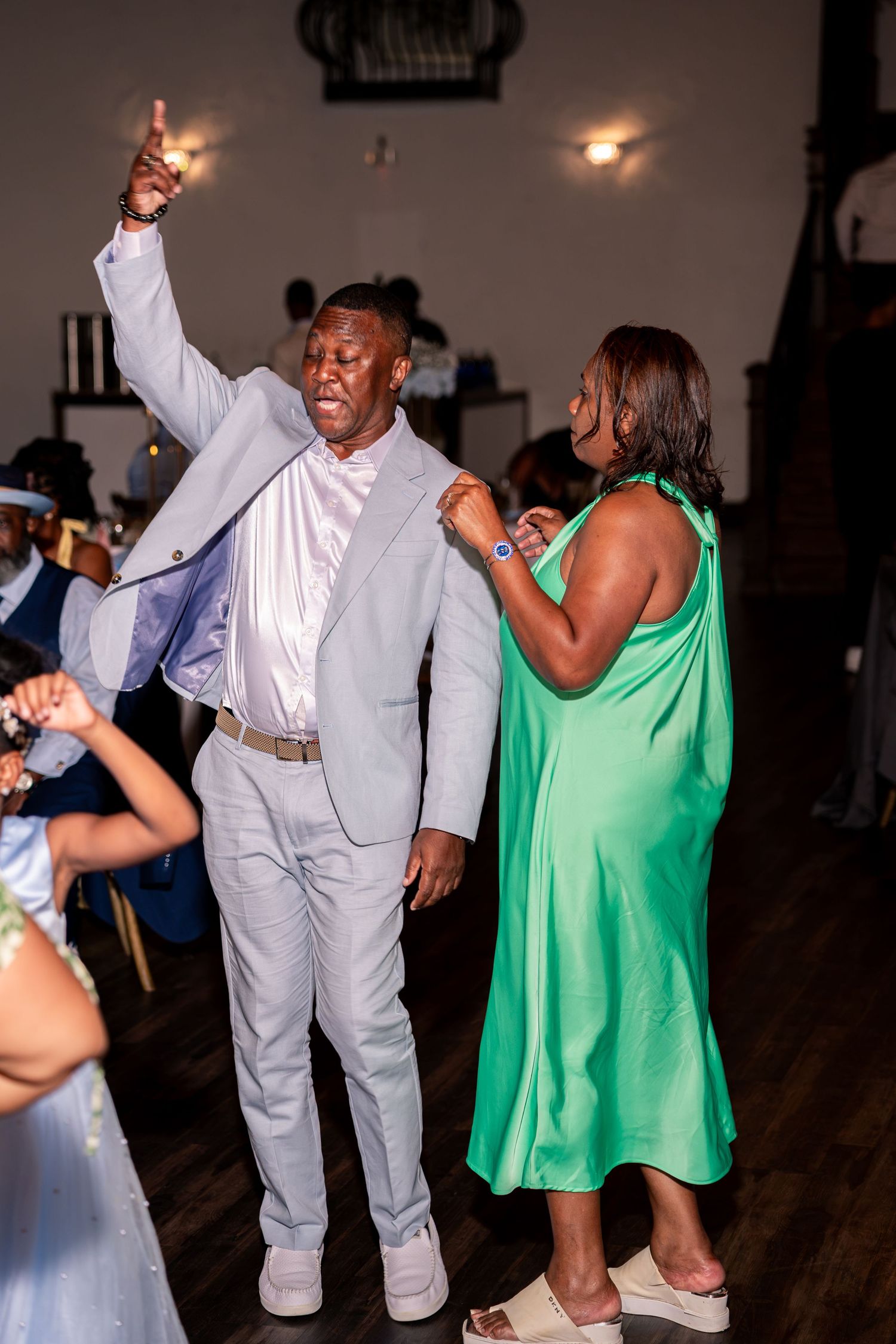 Man in gray suit dancing with woman in green dress at lively wedding reception.