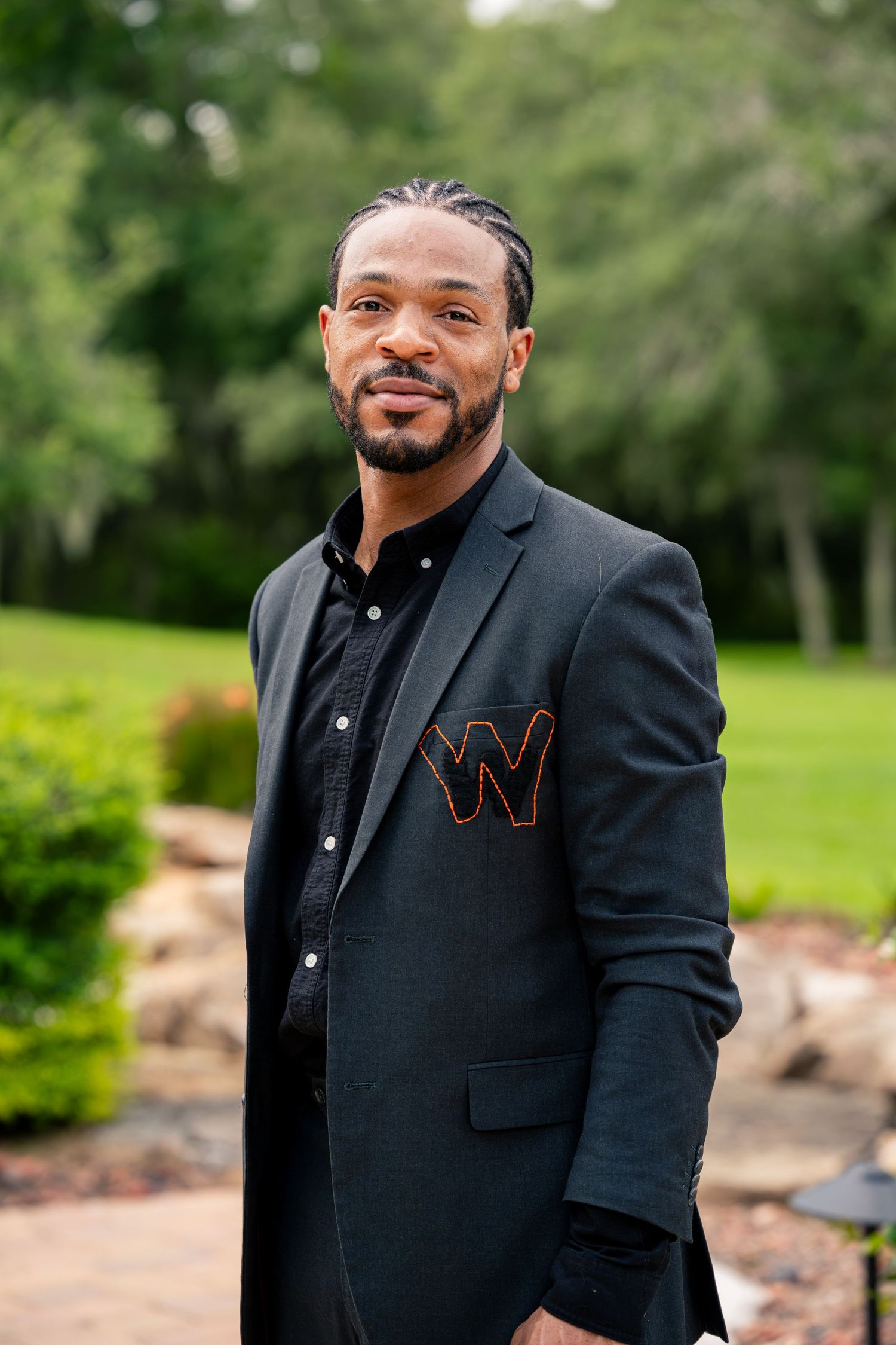 Man in black blazer with W emblem posing outdoors at a wedding venue.