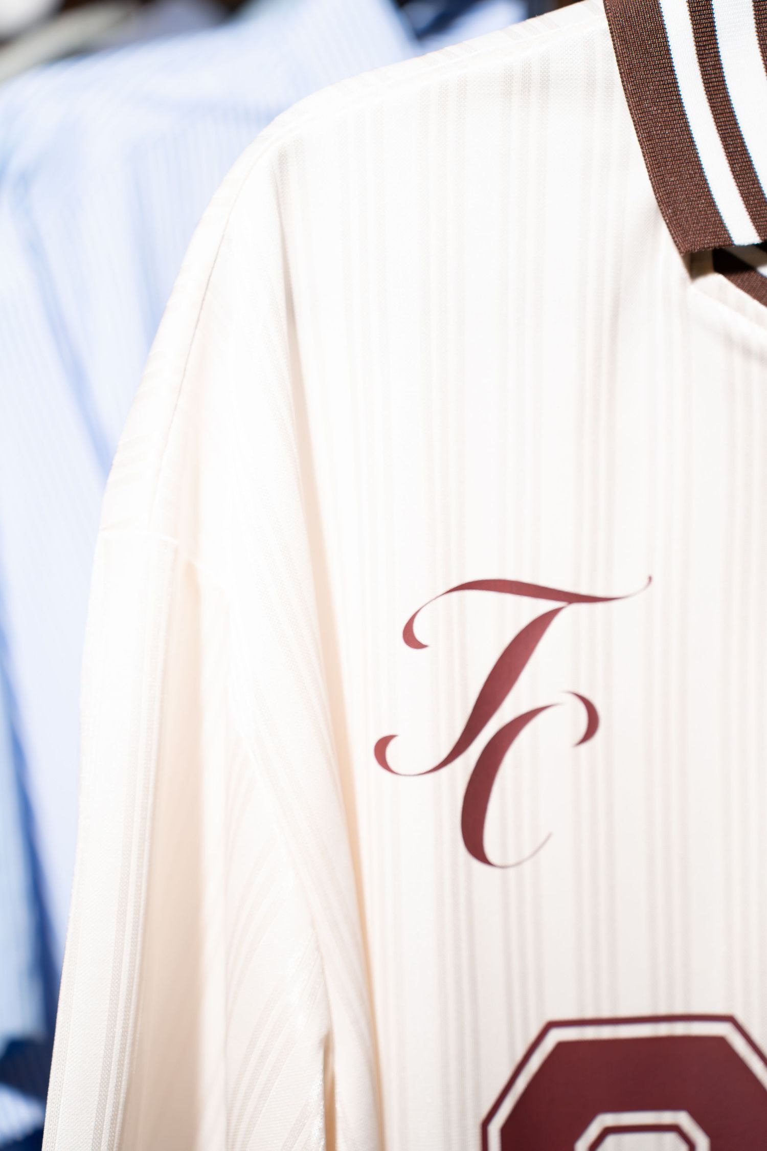 Close-up of cream pinstripe jersey with TC cursive logo on clothing rack.
