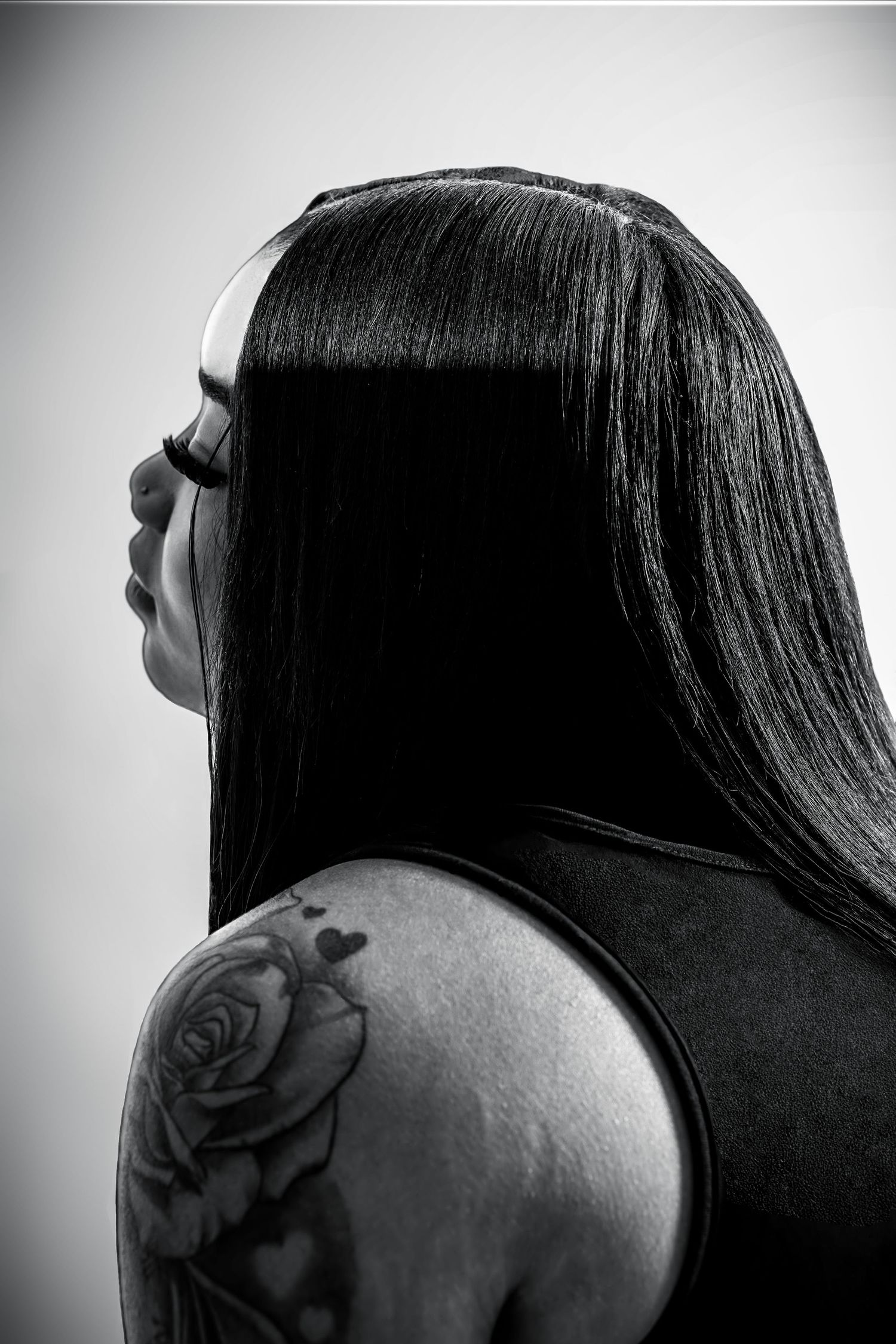 Black and white profile portrait of a woman with long straight hair and a rose tattoo on her shoulder.