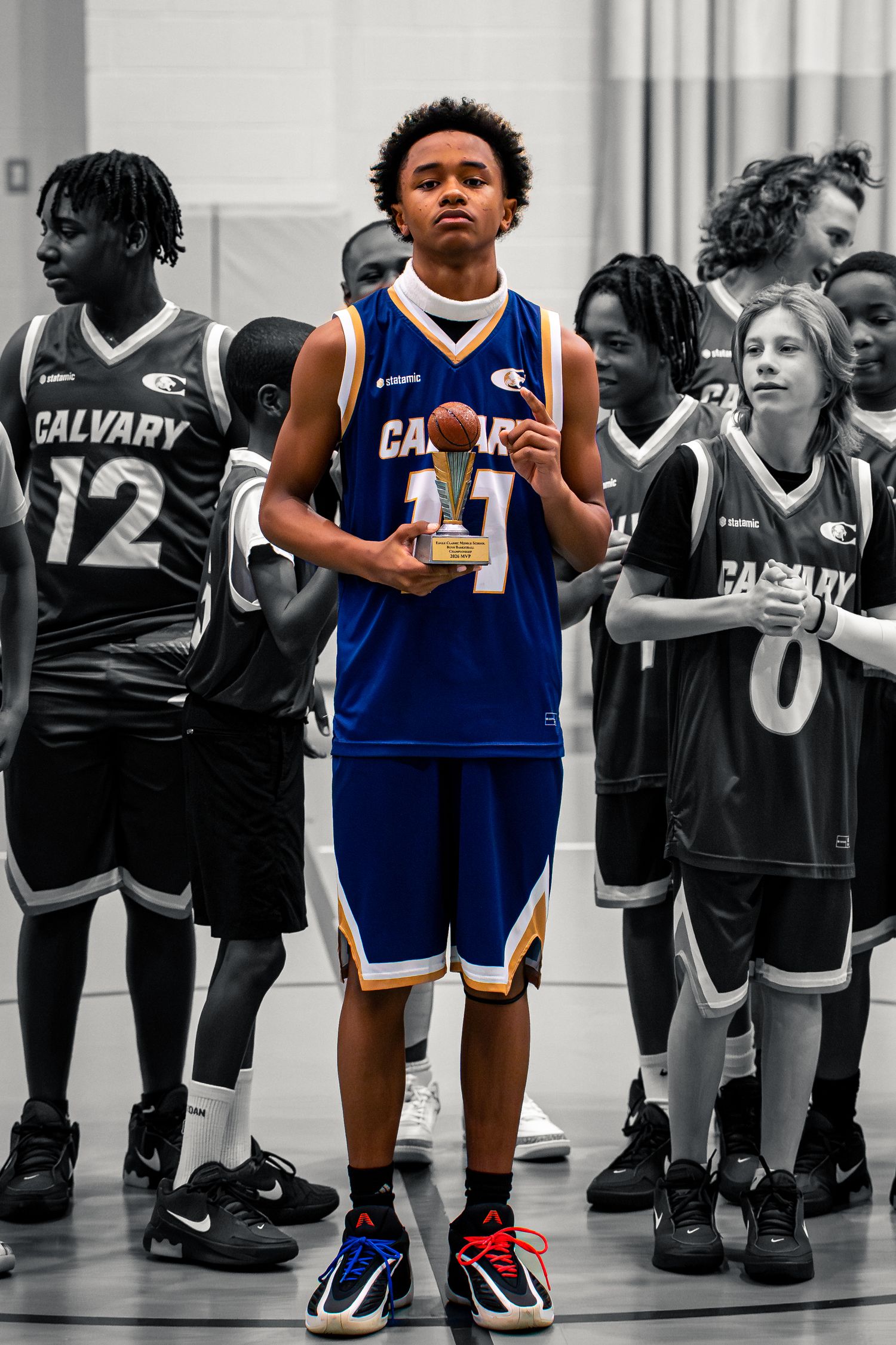 Calvary basketball player #11 holds trophy in selective color photo after tournament championship win.