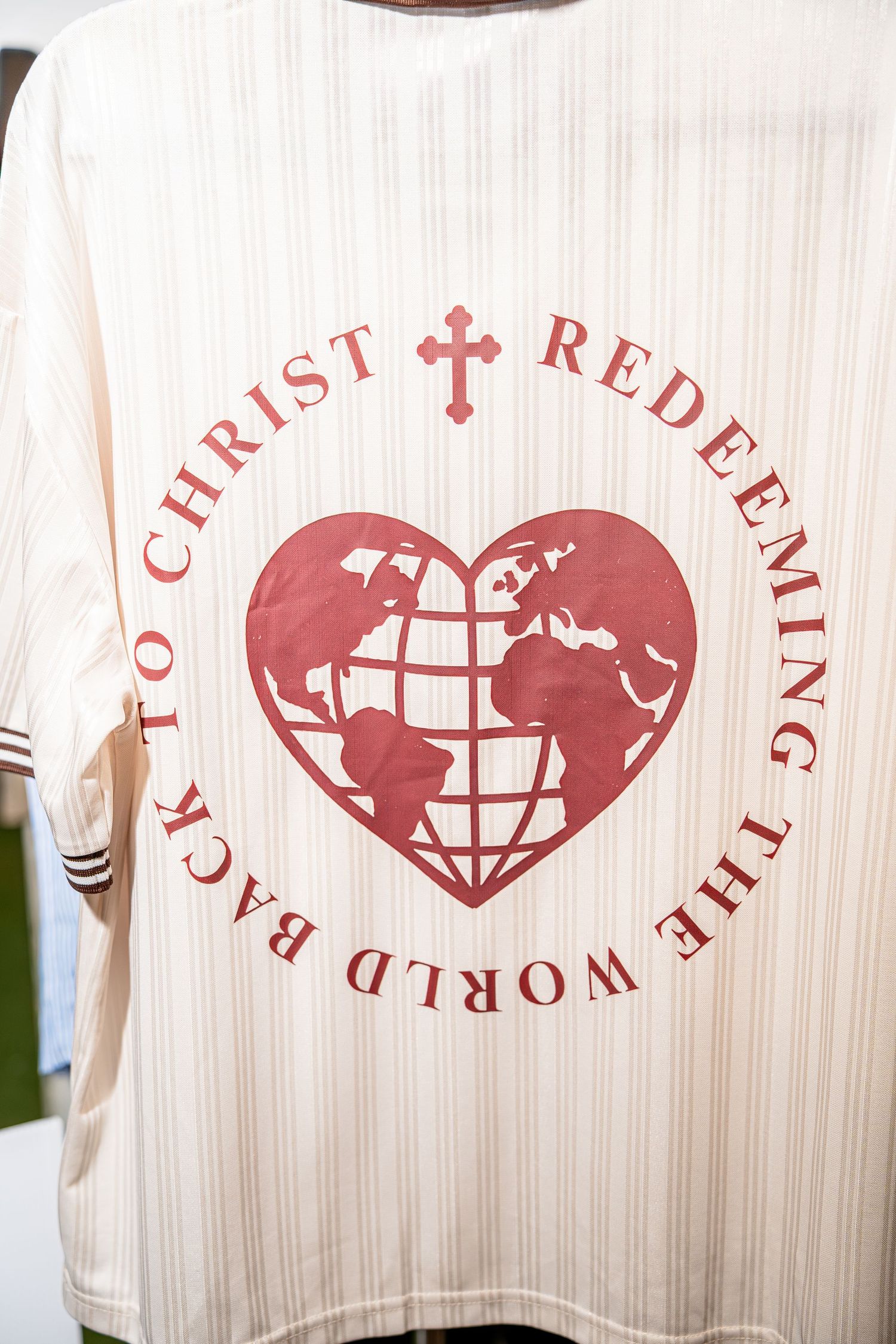 Back of cream jersey reading Redeeming the World Back to Christ with globe heart graphic.