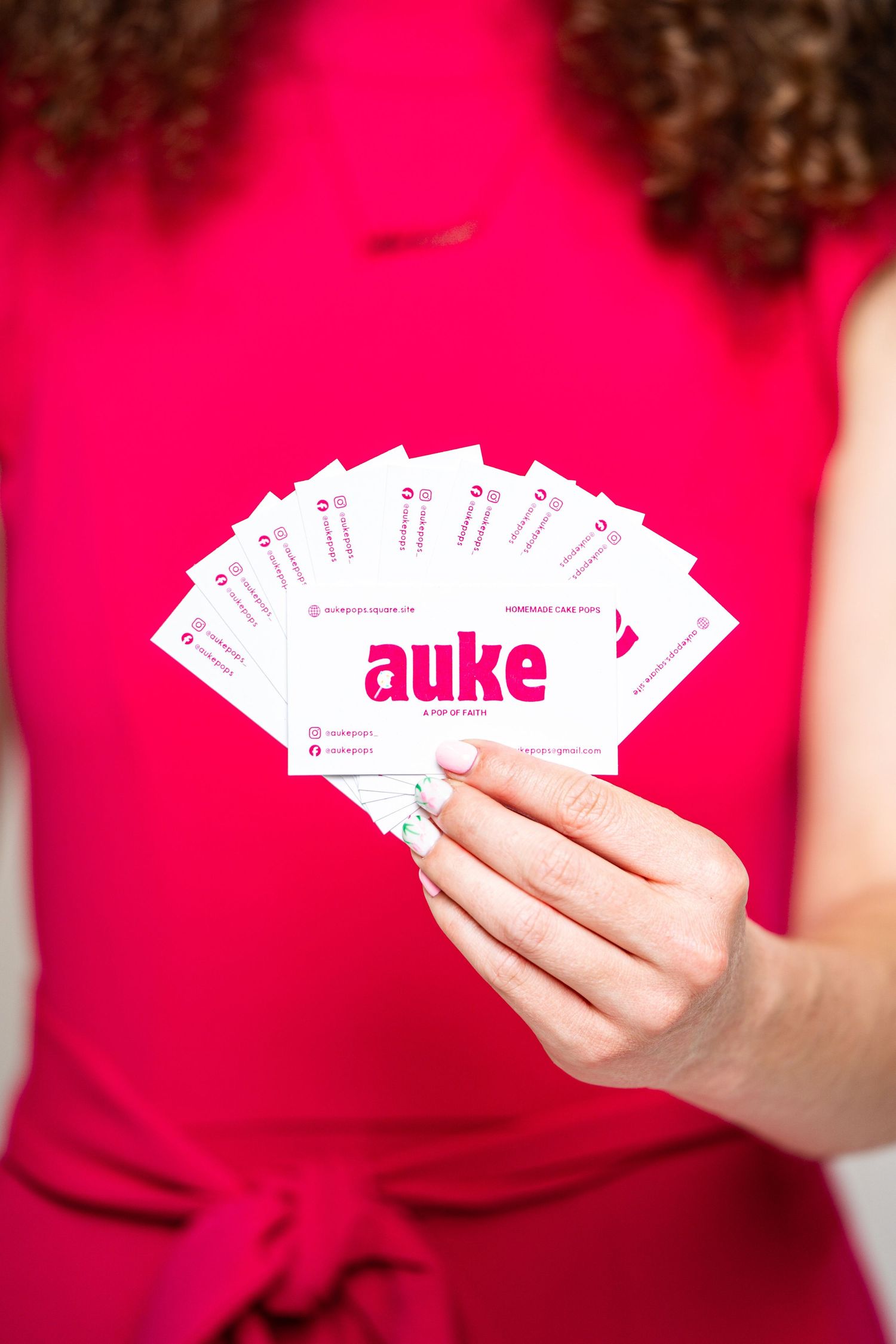 Woman in pink dress holding a fan of Auke pop-up cafe business cards toward the camera.