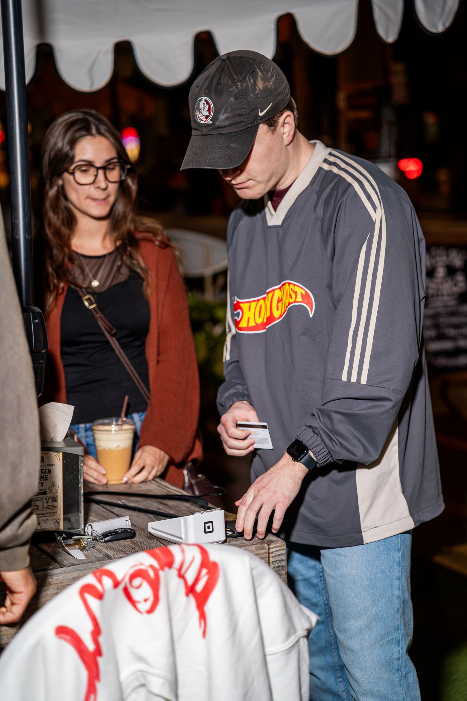 Man in Hot Ghost graphic jersey processing payment at outdoor clothing pop-up shop.