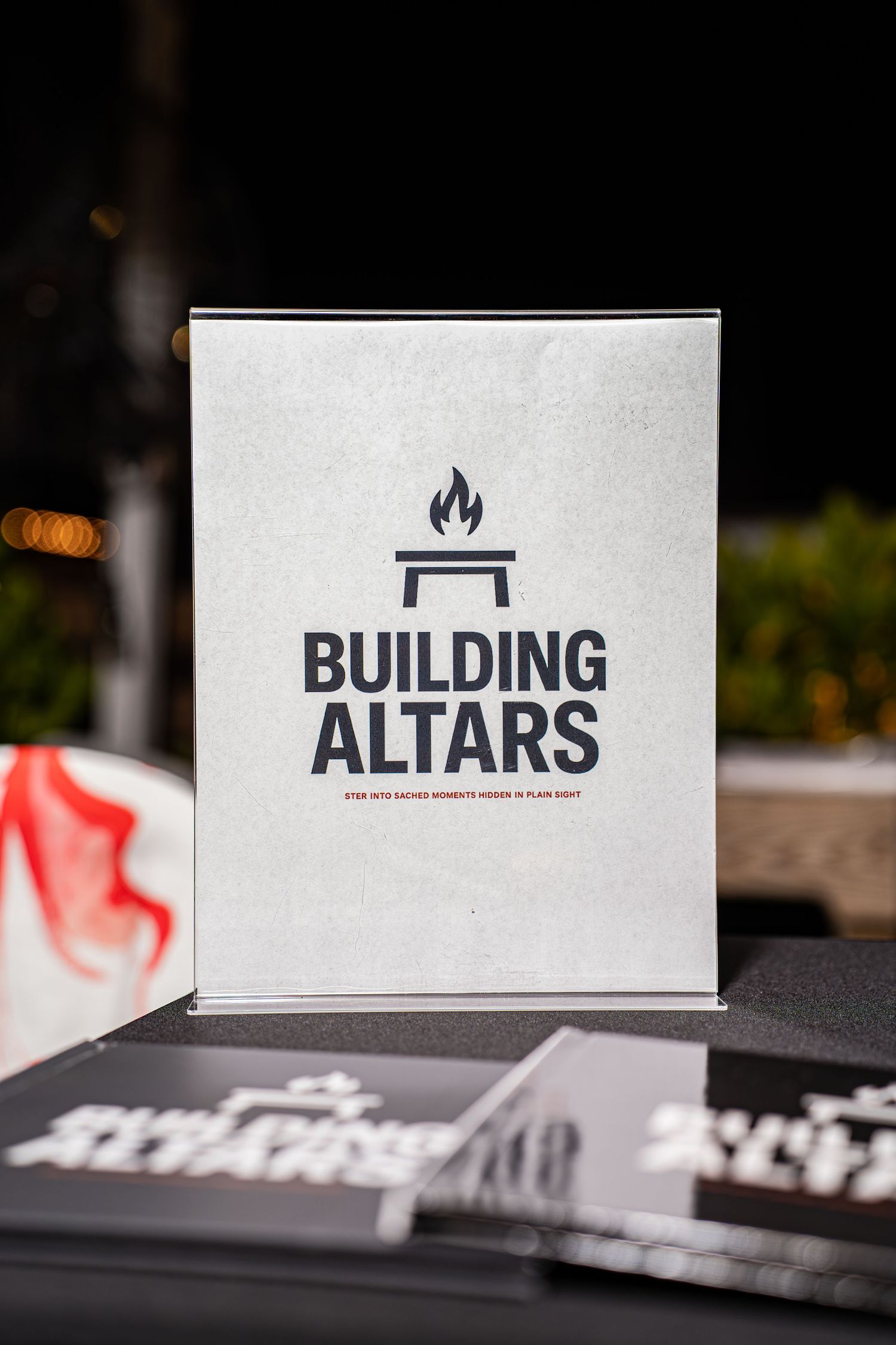 White Building Altars book displayed on table at outdoor event booth at night.