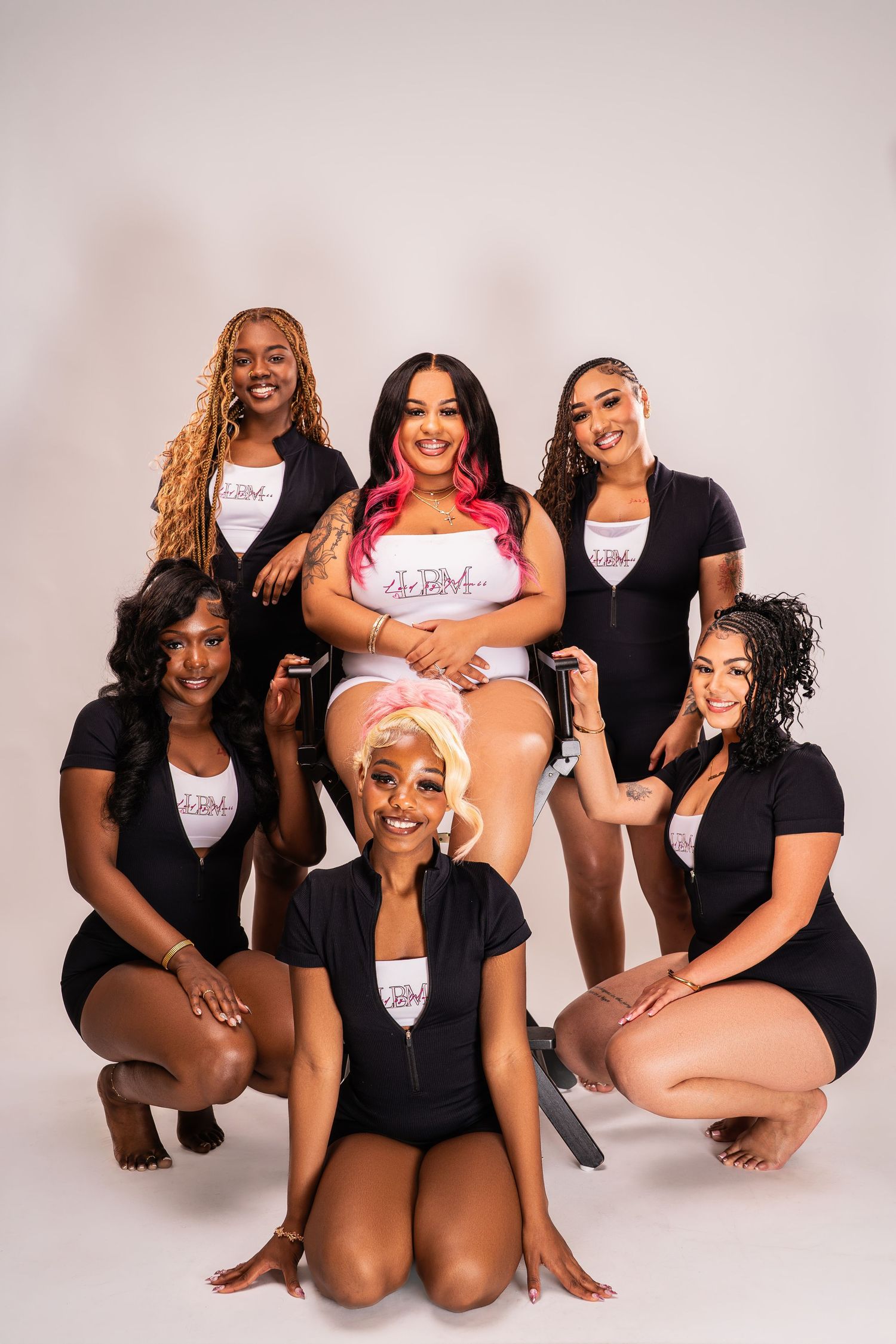 Seven Black women smiling in coordinated black outfits with one woman in white center top.