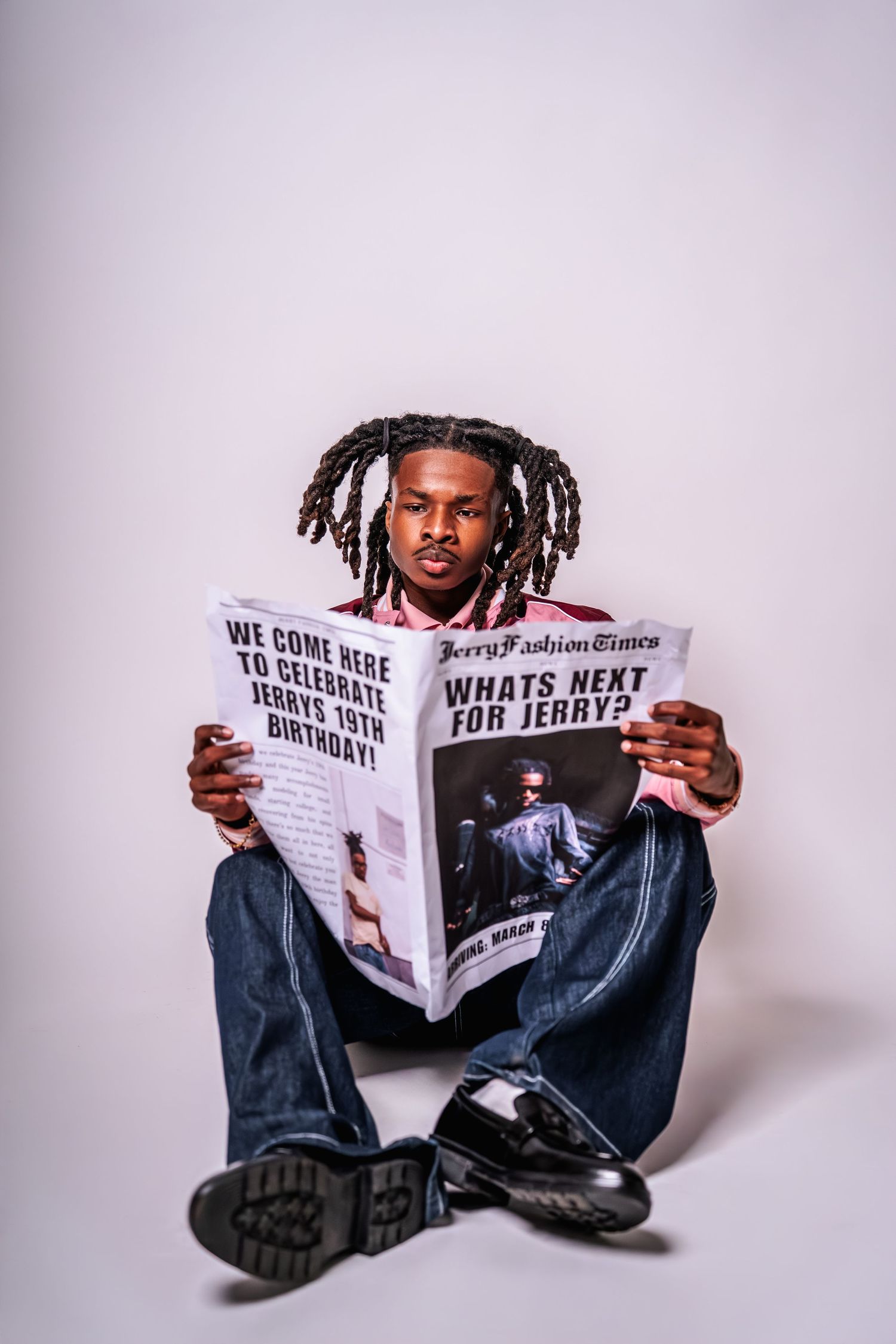 Young man with dreadlocks sitting on floor reading a custom newspaper headline about Jerrys 19th birthday celebration.