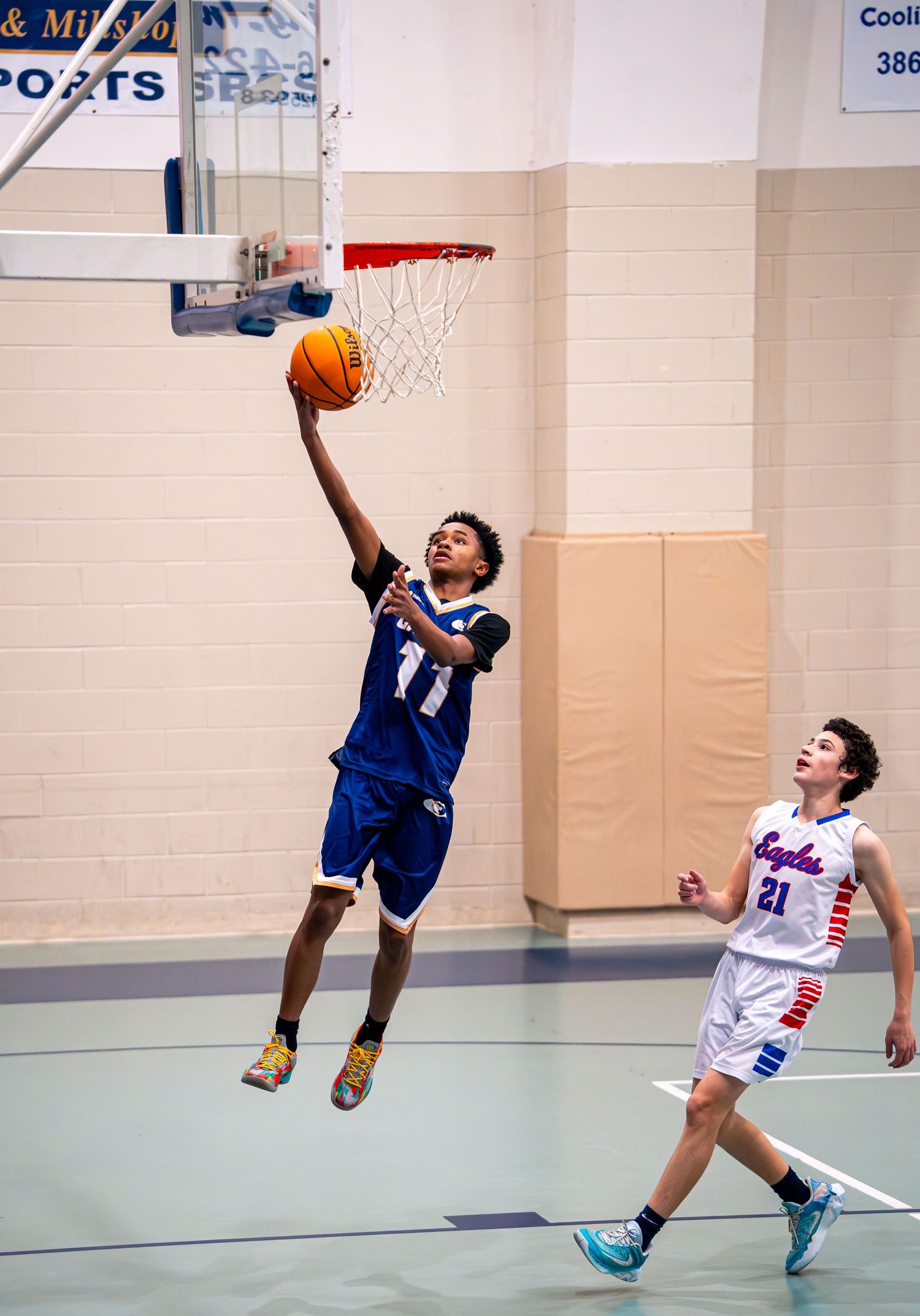 Basketball player #11 in blue Calvary jersey leaps for layup as defender watches during game.