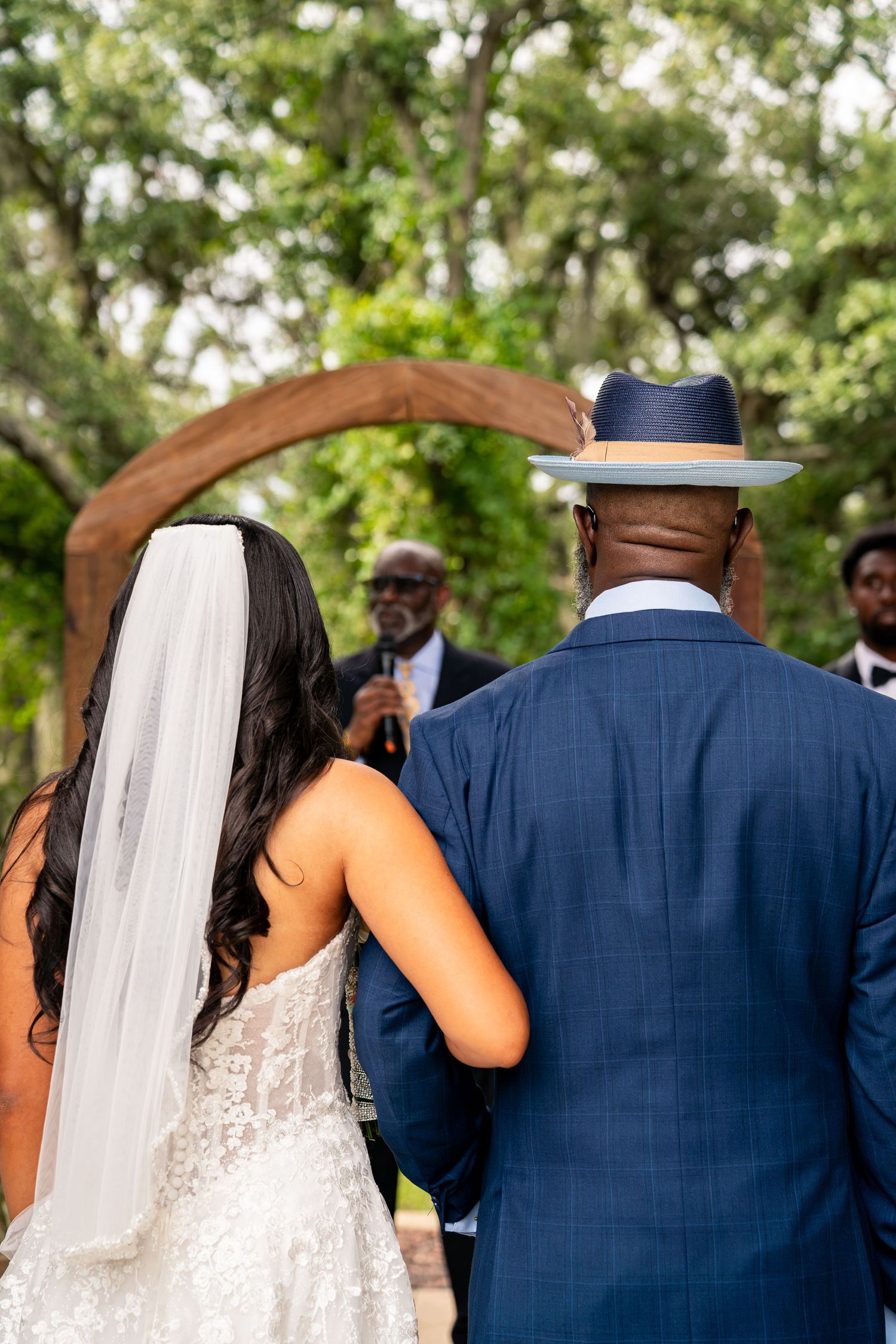 Bride and groom standing before officiant under wooden arch at outdoor wedding ceremony.