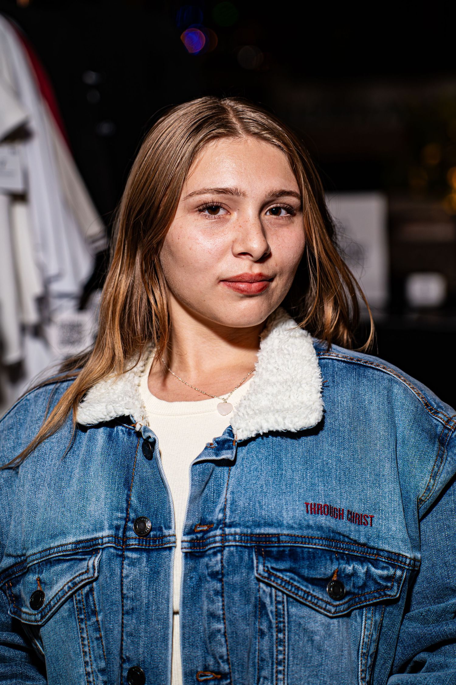 Young woman in denim sherpa jacket with Through Christ Brand logo at outdoor event.