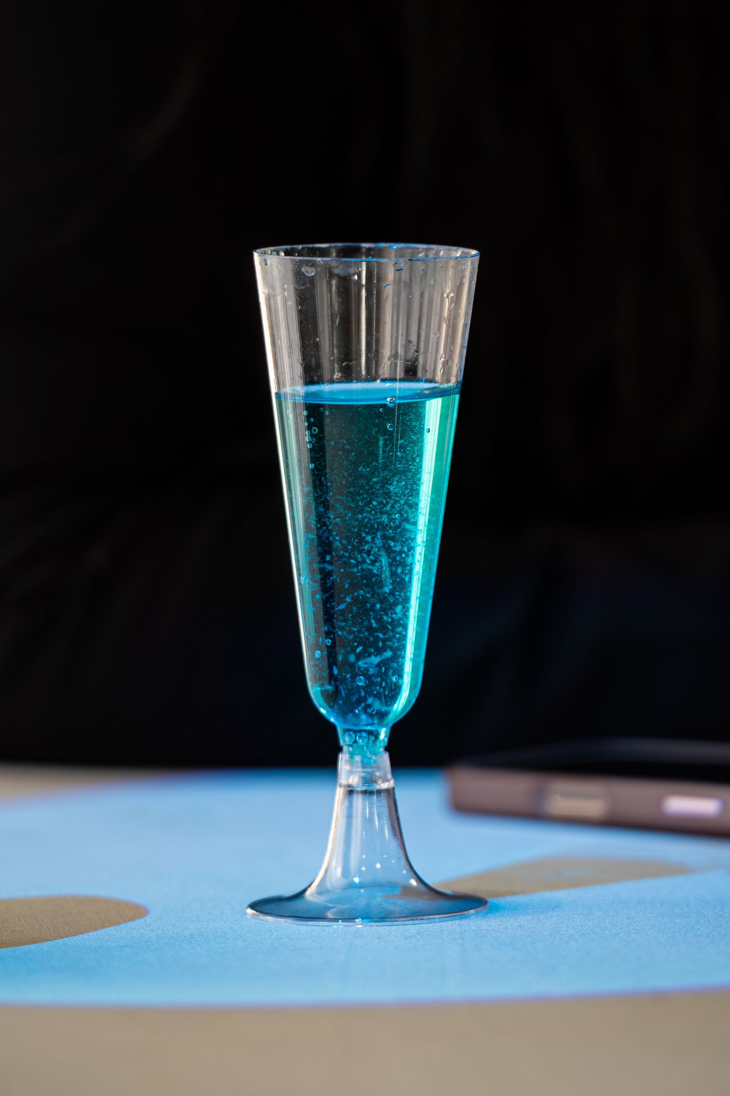 Blue sparkling beverage in clear champagne flute on light blue surface.