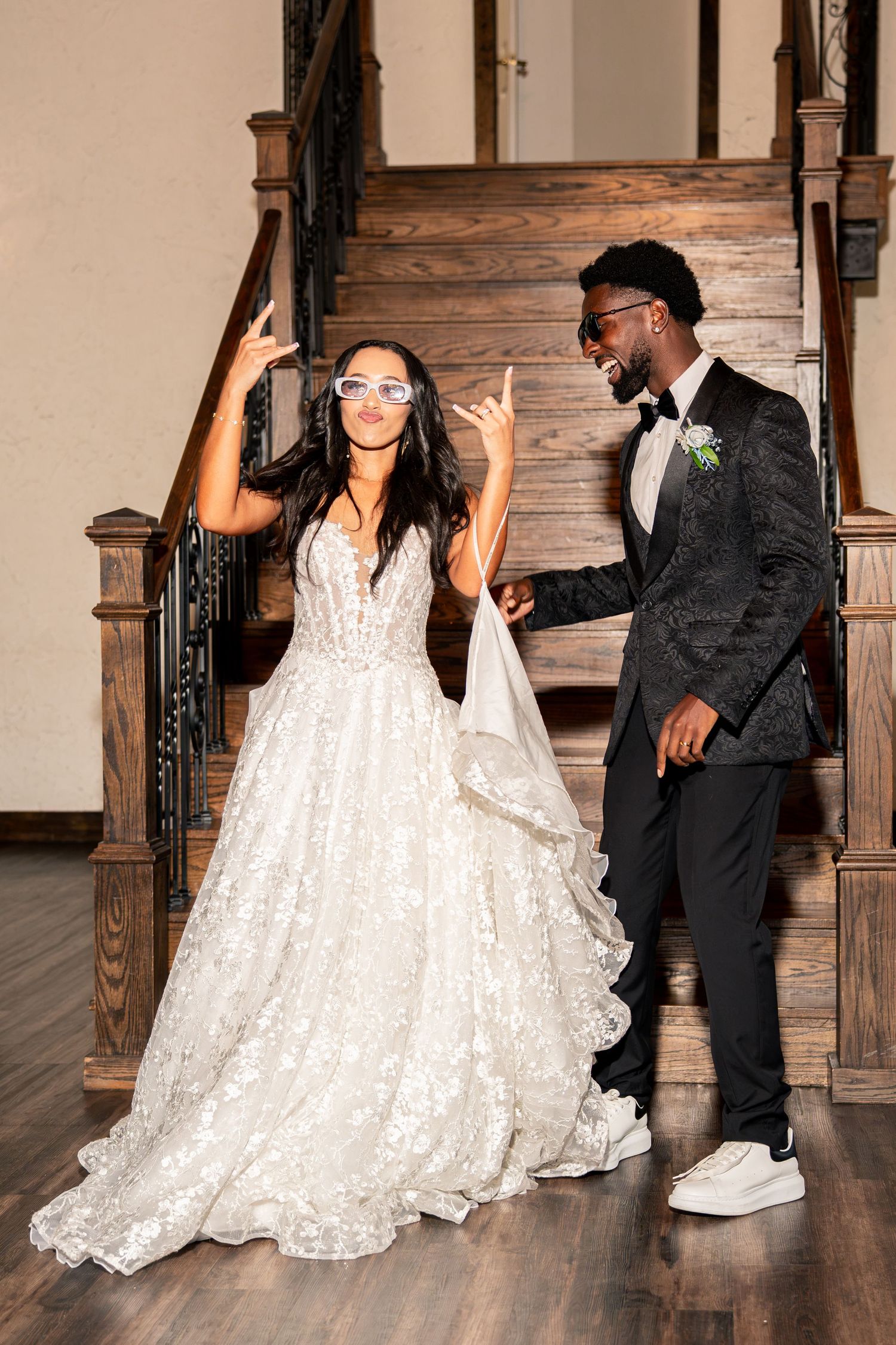 Joyful bride in sparkly ballgown and groom in black tuxedo celebrate on staircase at wedding reception.