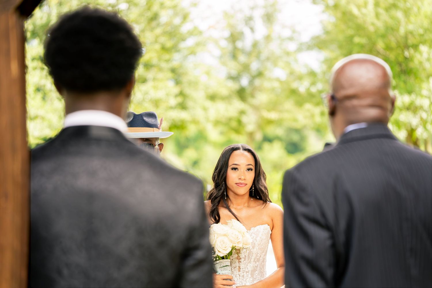 Bride walking down the aisle holding white roses at an outdoor wedding ceremony.