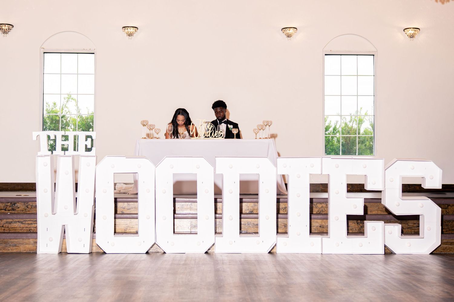 Newlyweds stand behind large white marquee letters spelling THE WOODIES at reception.