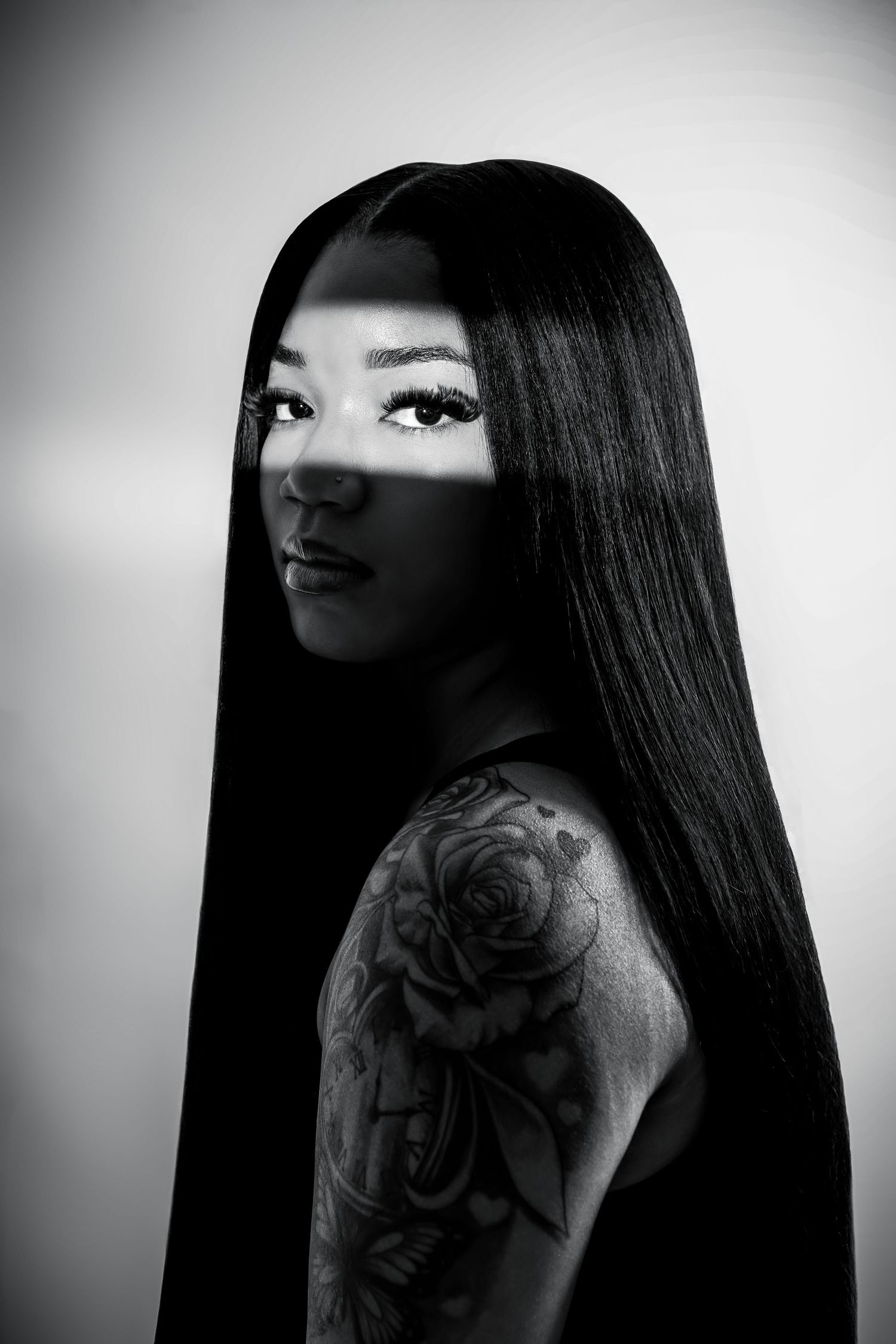 Black and white portrait of woman with long straight hair and floral rose shoulder tattoo.