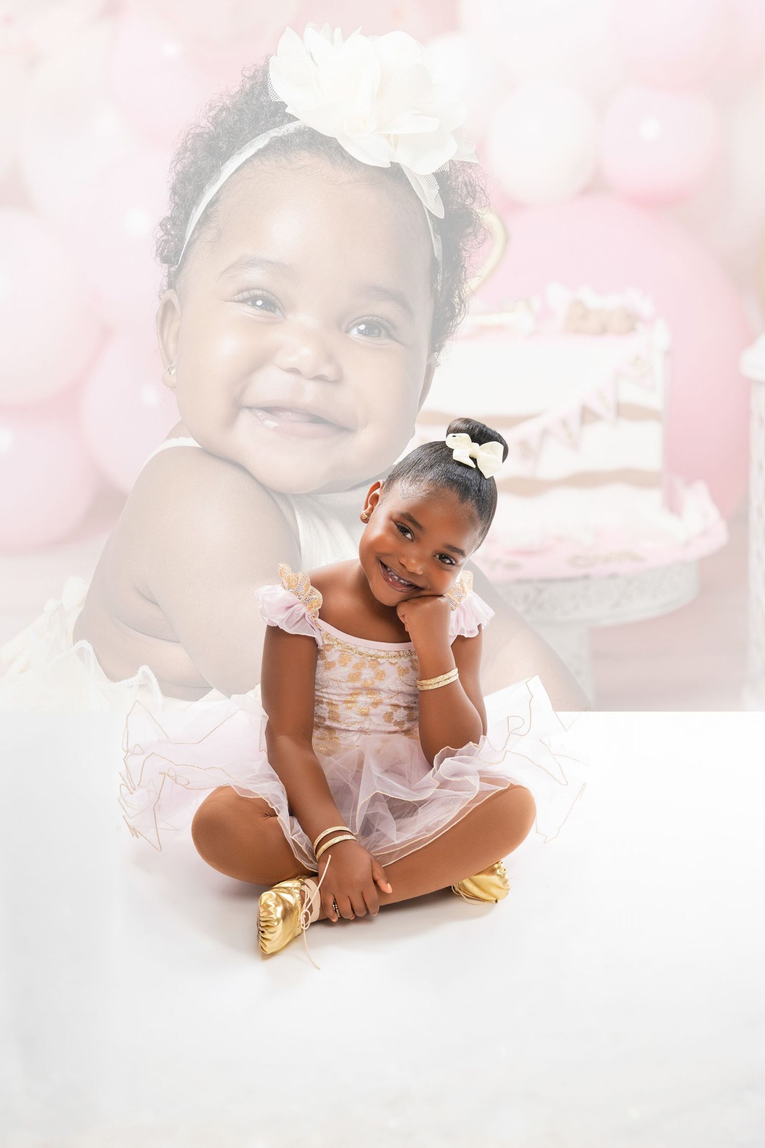 A young girl in a pink tutu dress and gold shoes sits cross-legged, smiling, with a baby photo backdrop behind her.
