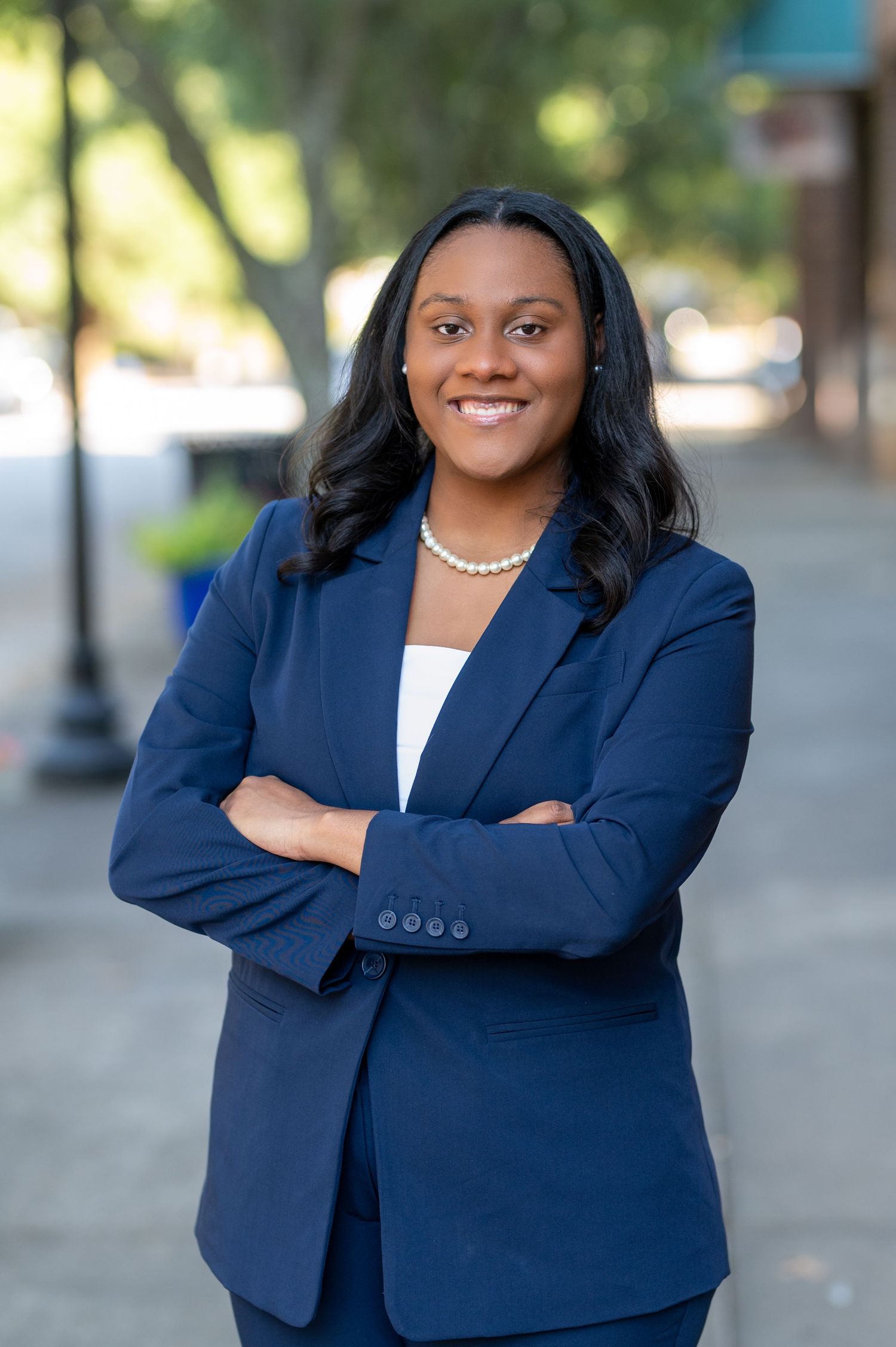 Professional portrait of woman in navy blazer and pearl necklace outdoors.