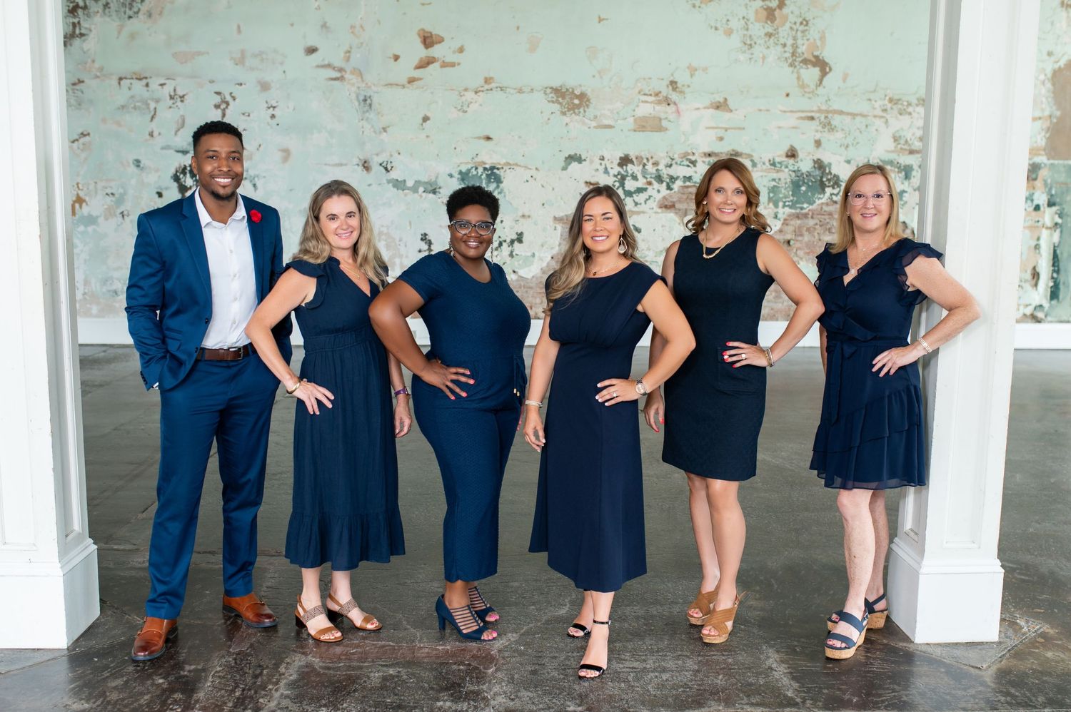Group of friends in coordinated navy blue and black outfits pose playfully against a white wall.