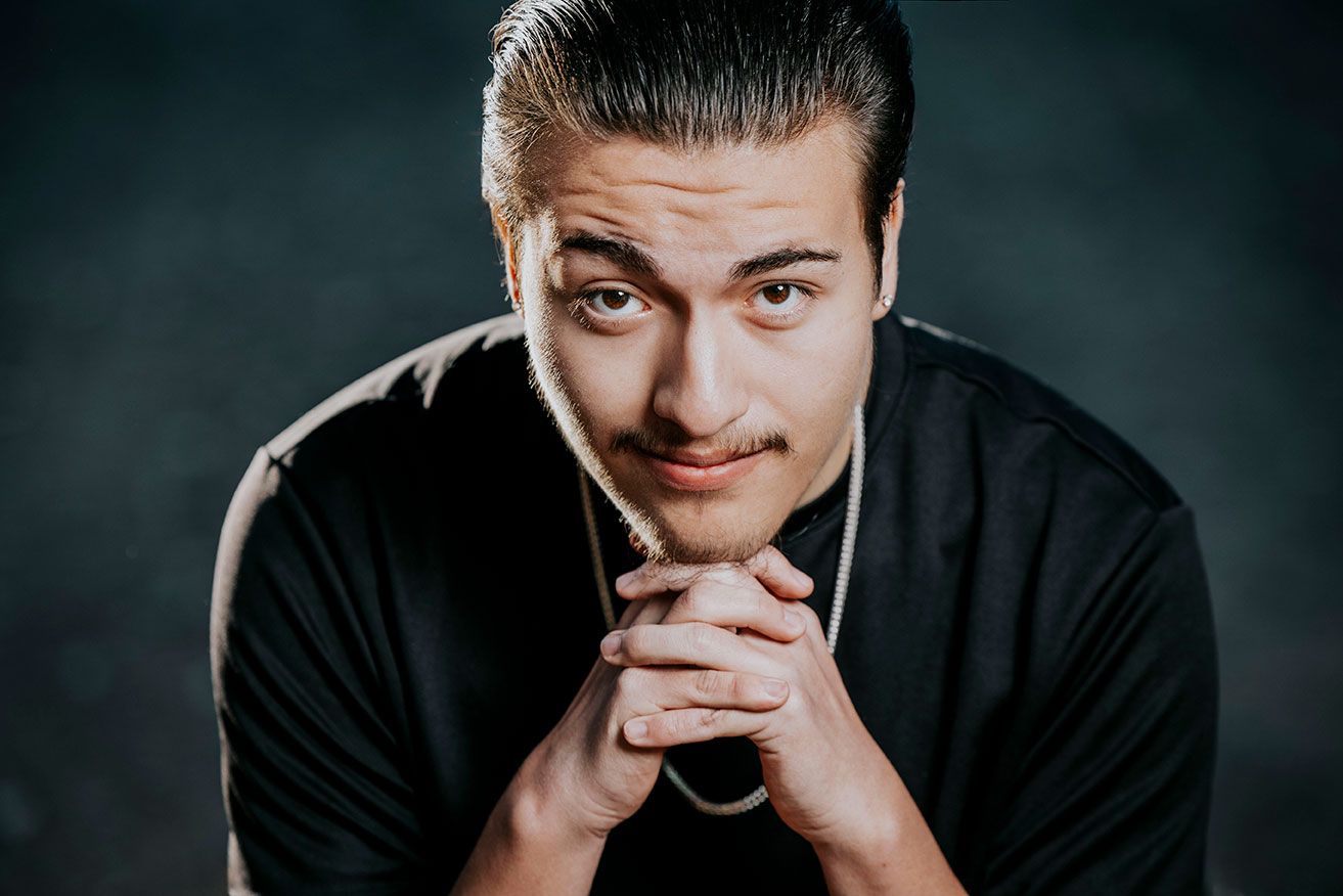 High School Senior Portrait of hispanic guy wearing black shirt leaning towards camera and chin resting on hands.