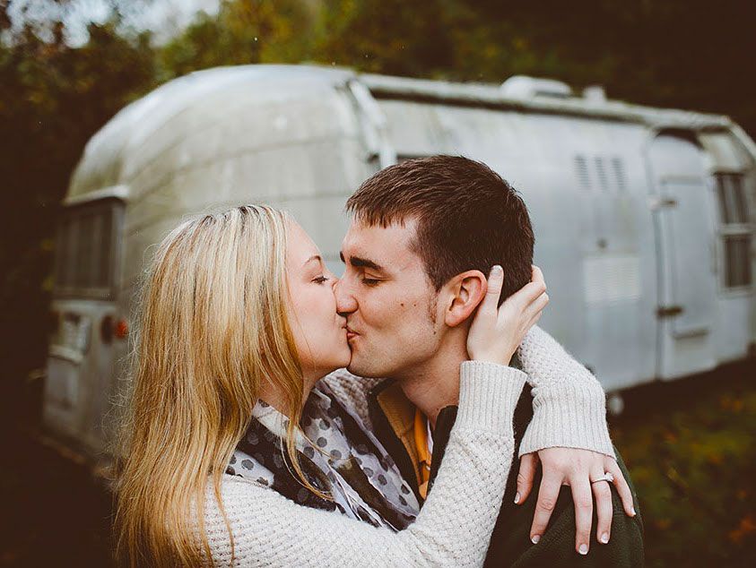Man and woman kissing in front of a camper.